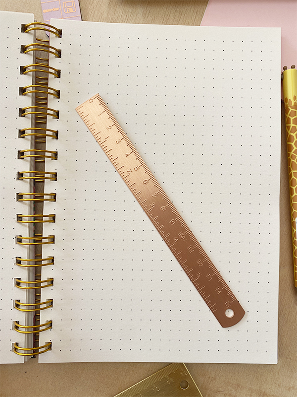 Caderno de argolas com régua metálica cobre e lápis amarelo com padrão de girafa