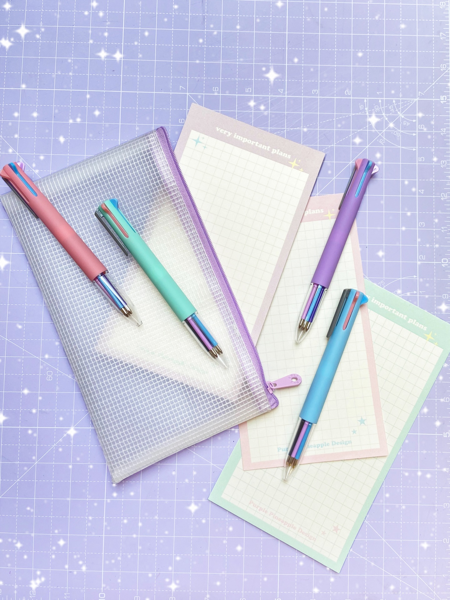 Estojo translúcido lilás, canetas coloridas pastel e blocos de notas quadriculados com títulos visíveis