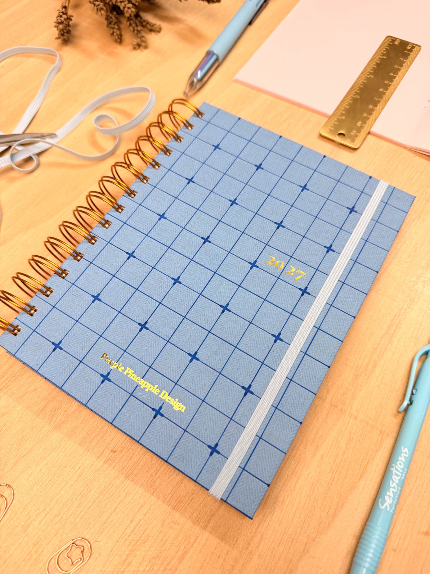 Caderno azul quadriculado com texto dourado e acessórios de escritório numa mesa