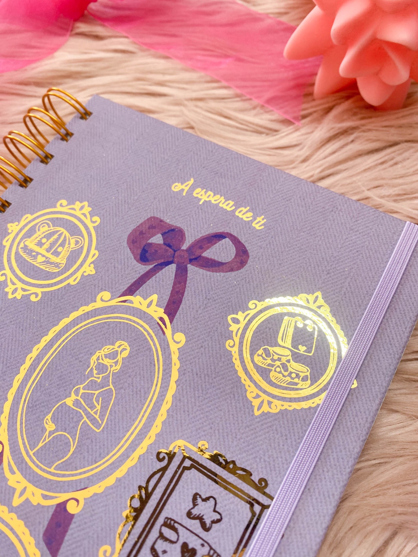 Caderno com capa cinzenta e detalhes dourados sobre pele sintética rosa