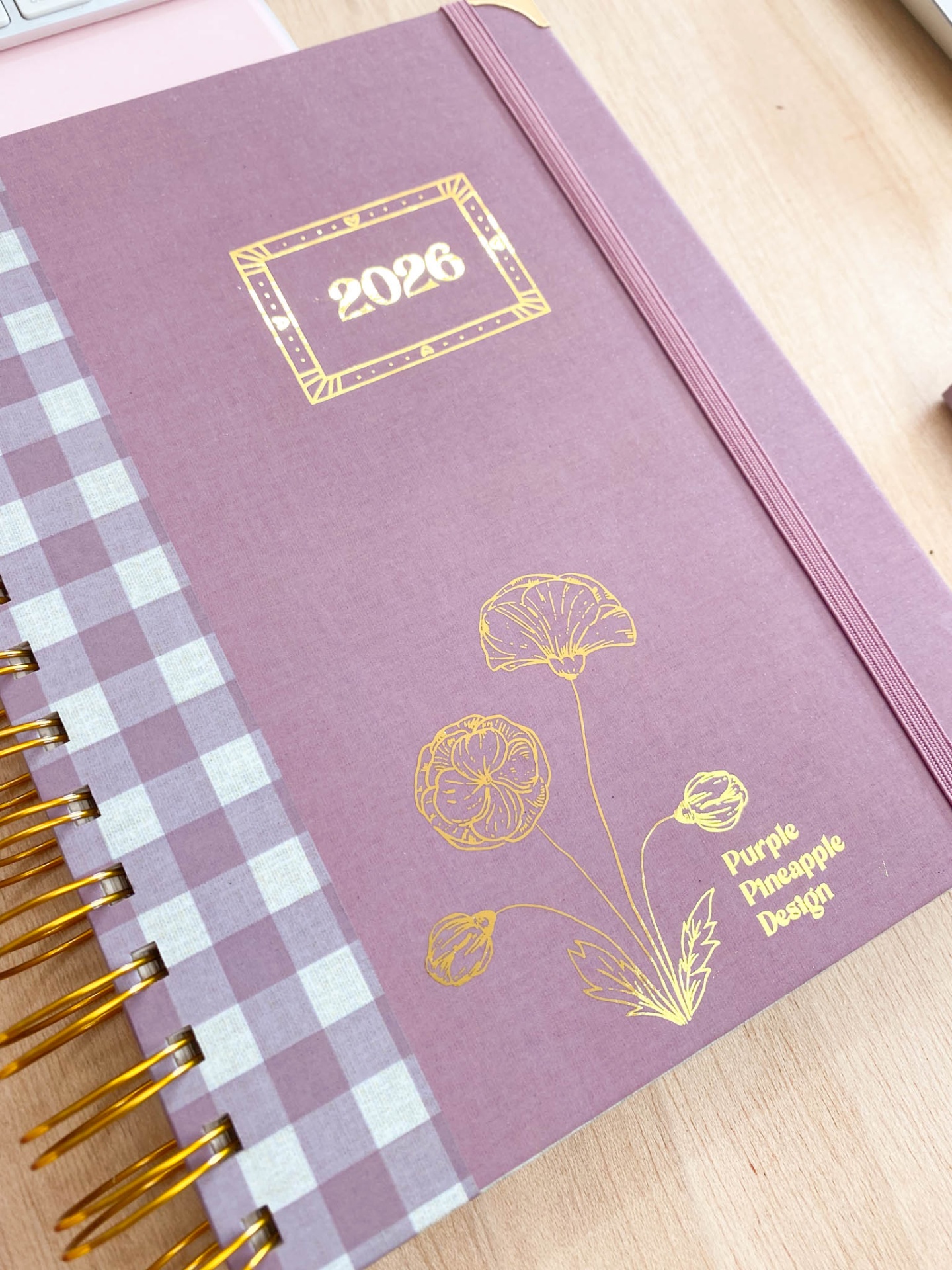 Agenda 2026 roxa com padrão xadrez, flores douradas e texto 'Purple Pineapple Design'