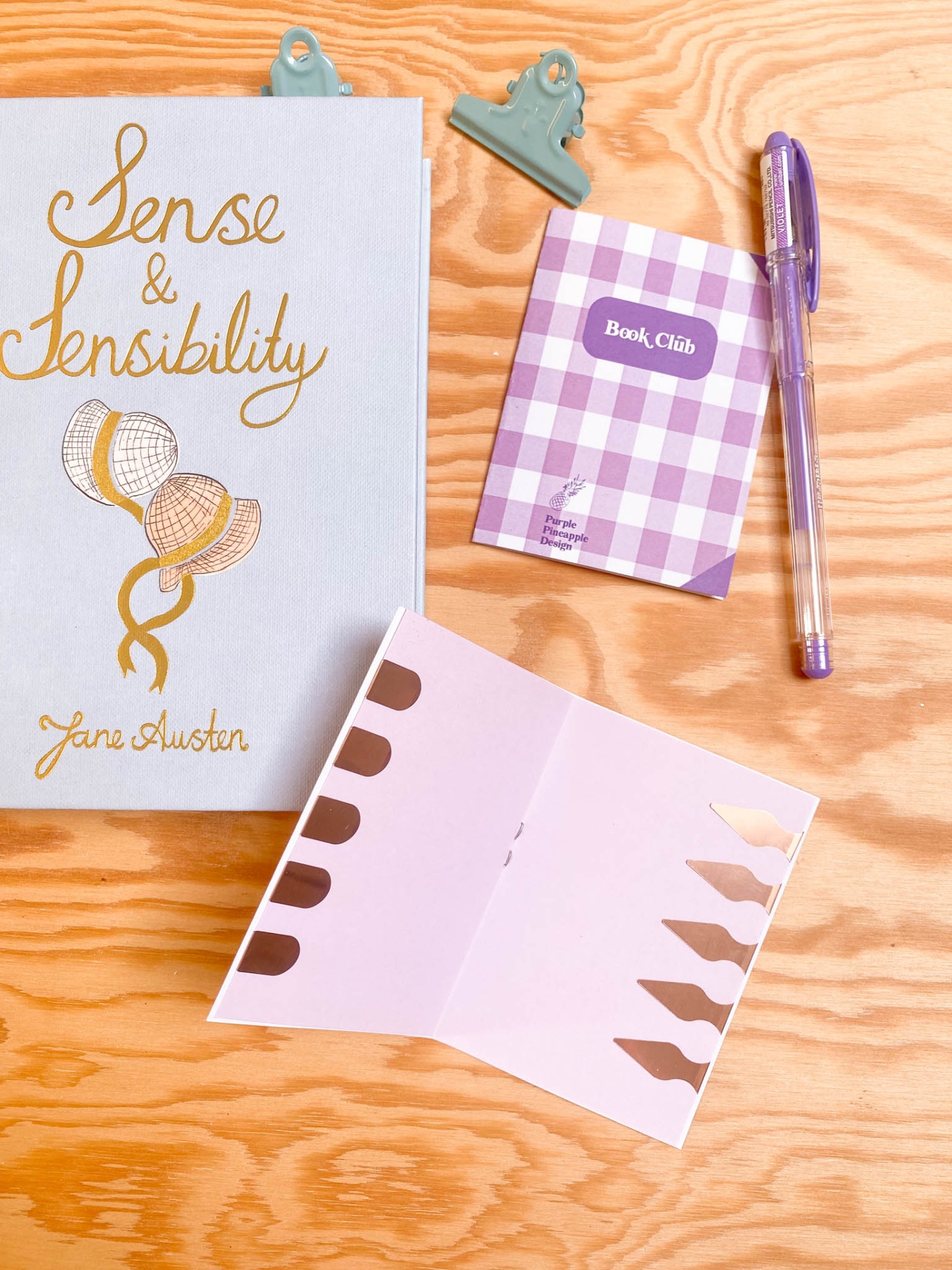 Livro, caderno, caneta, clips e etiquetas sobre mesa de madeira