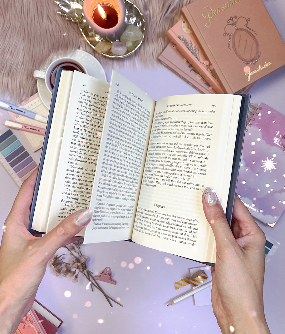 Livro aberto segurado por mãos femininas com decoração, com chá, vela e livros ao fundo