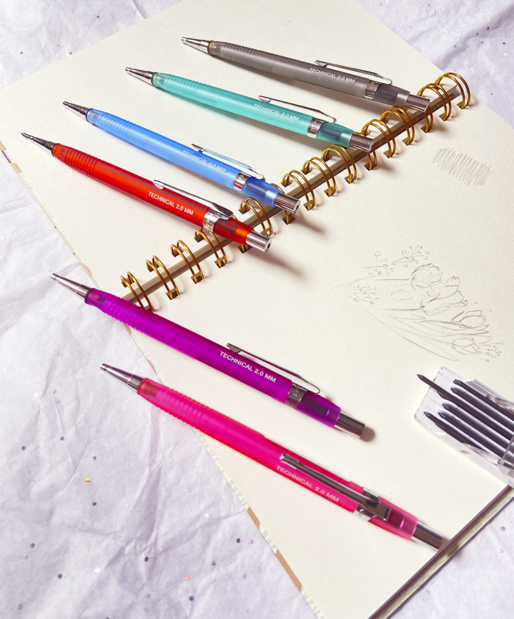 Seis canetas técnicas coloridas sobre caderno de espiral com desenhos à mão.