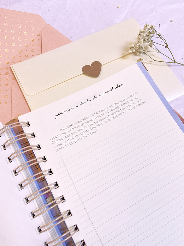 Agenda espiral aberta ao lado de envelopes e uma pequena flor branca