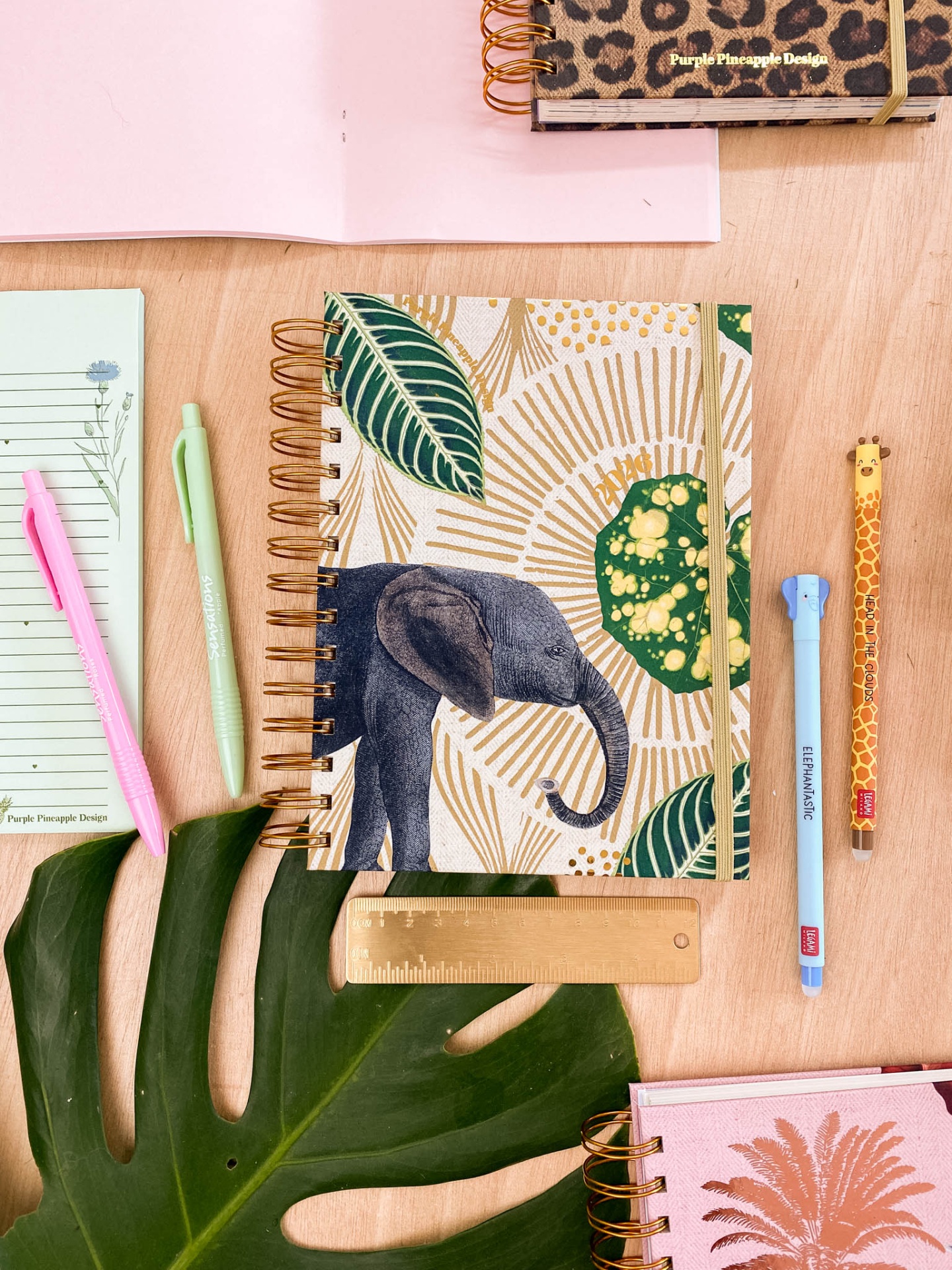Caderno com capa de elefante e canetas coloridas sobre mesa de madeira clara