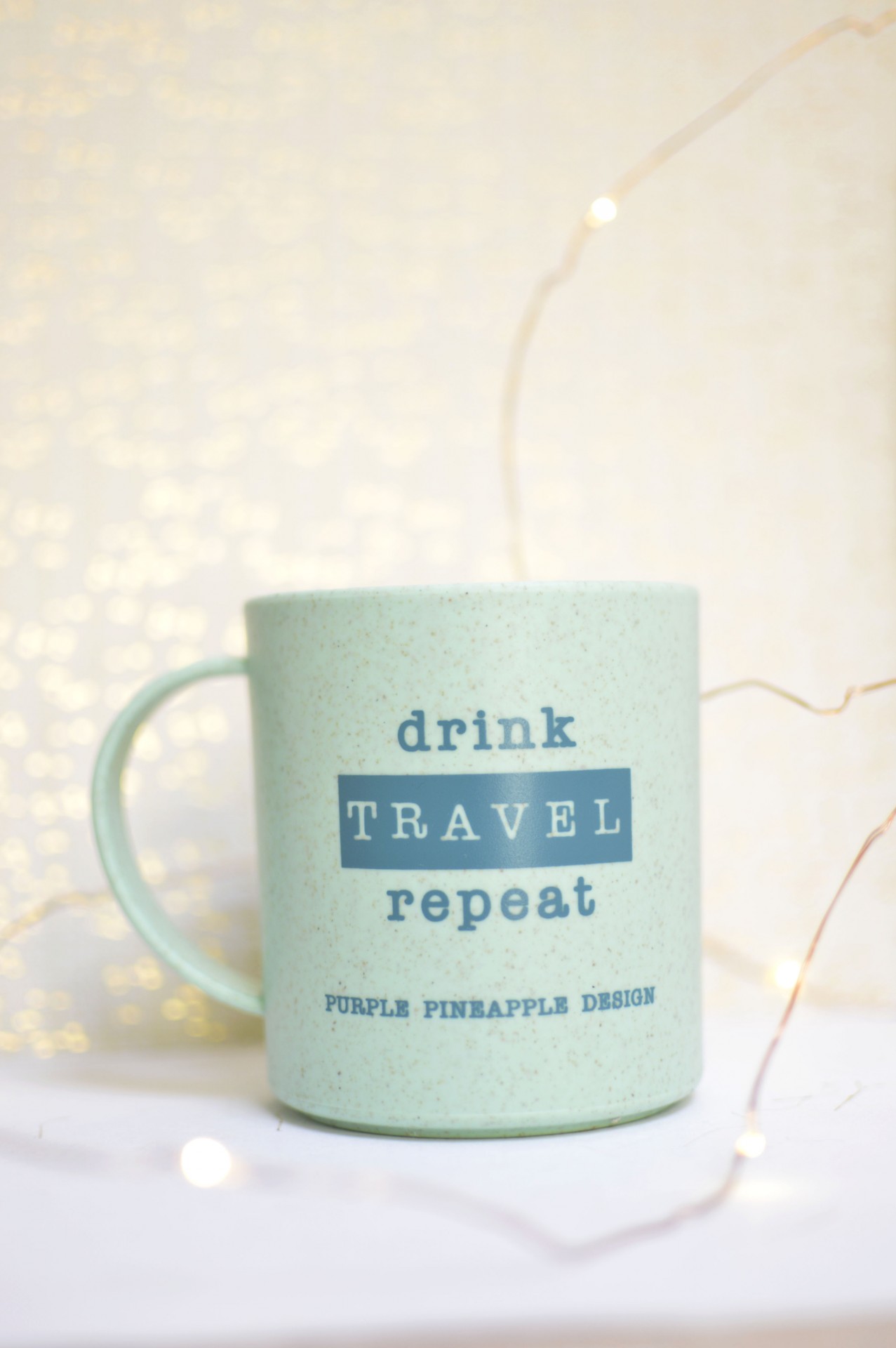 Caneca verde pálido com texto azul sobre fundo claro com luzes desfocadas