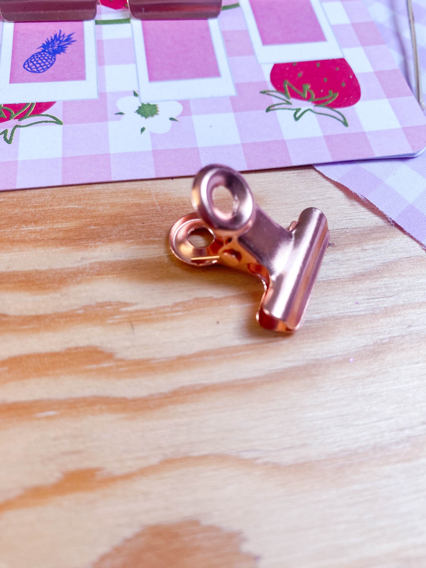 Clipe metálico cobre sobre mesa de madeira com papel quadriculado rosa e branco ao fundo