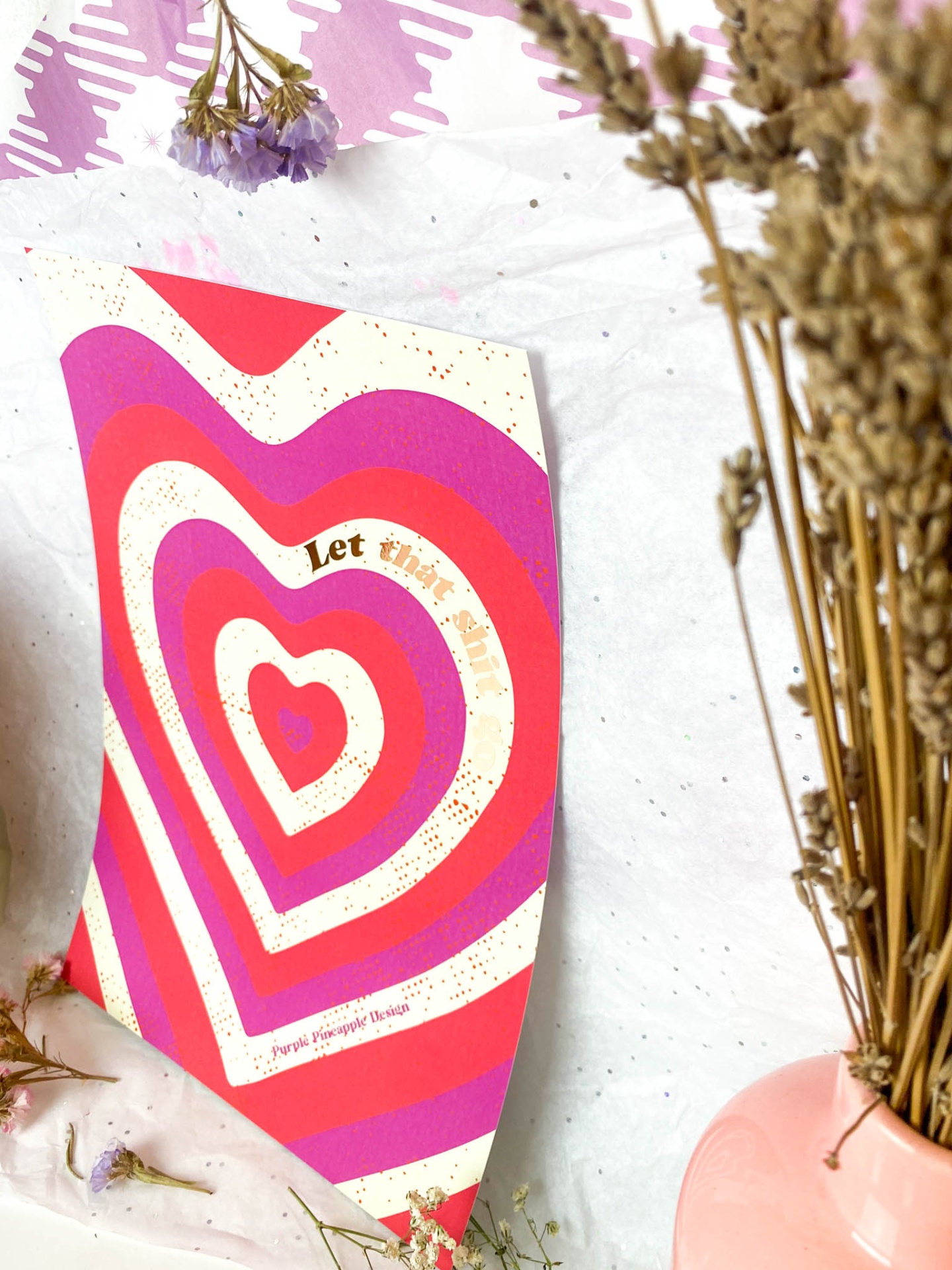 Cartaz colorido com corações em rosa, vermelho e branco com texto dourado, flores secas em vaso cor de rosa