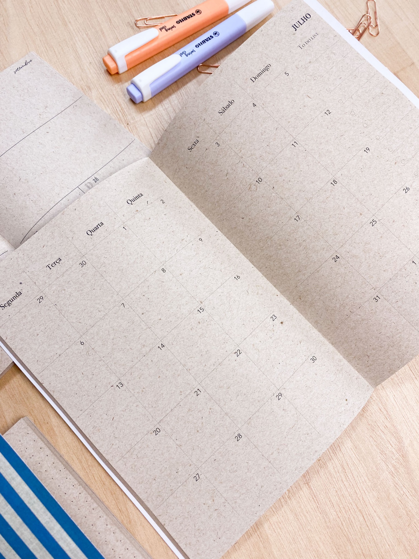 Agenda com calendário mensal aberto ao lado de marcadores de texto sobre mesa de madeira