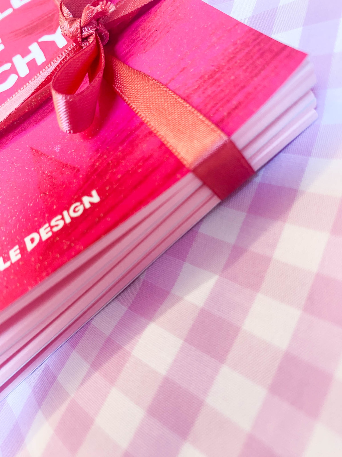 Livro vermelho com fita de cetim sobre tecido xadrez lilás e branco