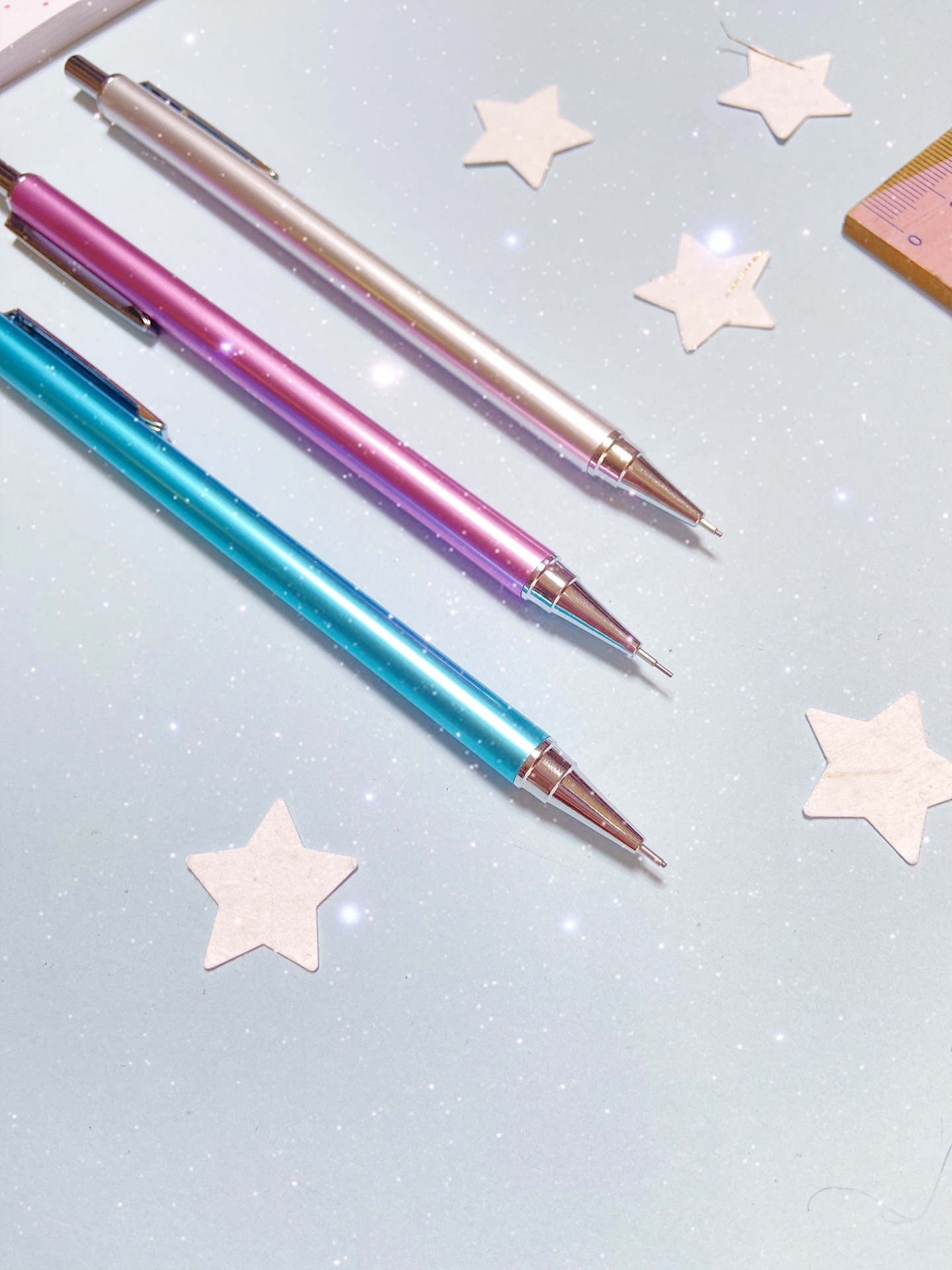Três lápis mecânicos metálicos coloridos e estrelas de papel