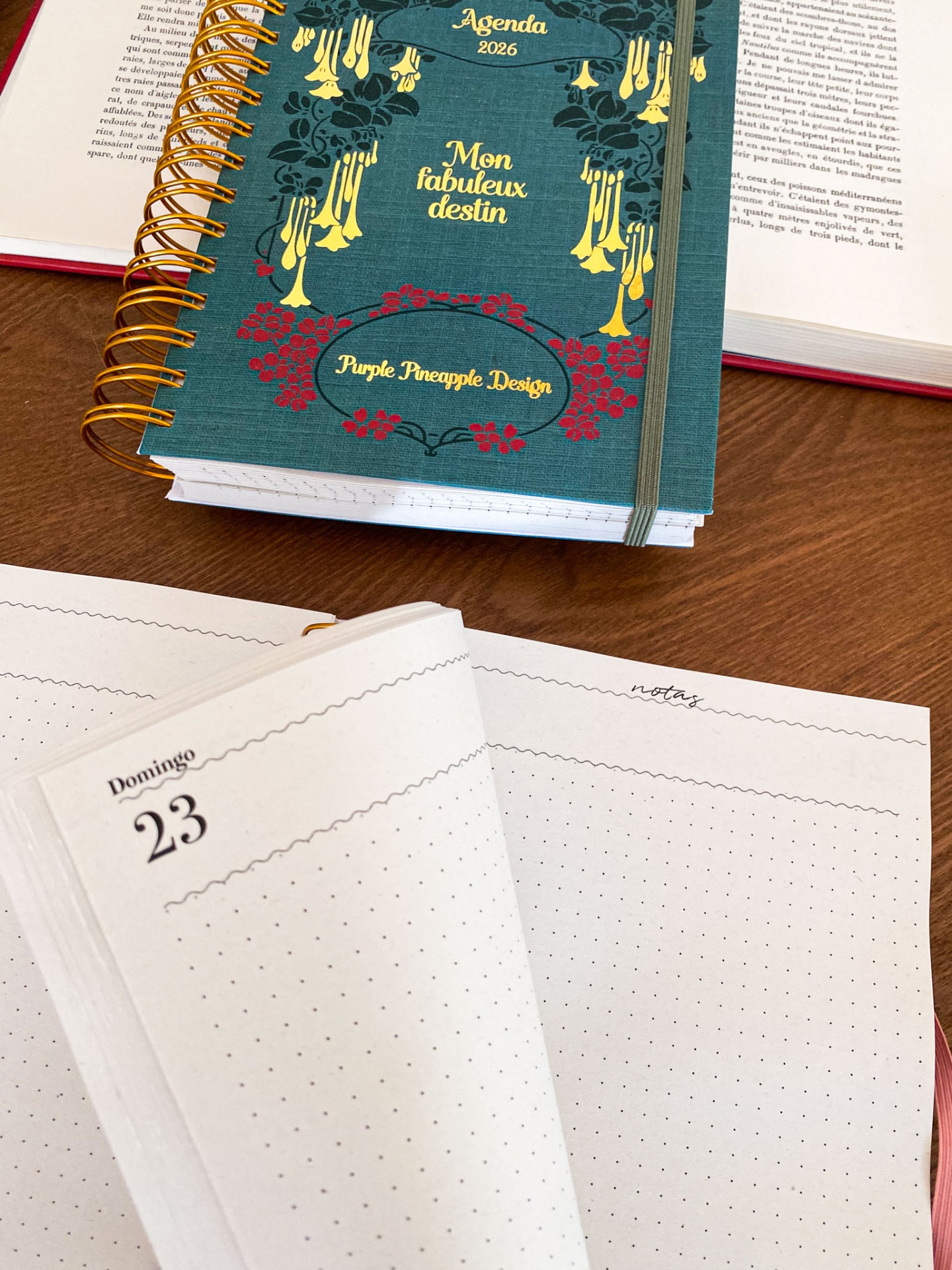 Agenda 2026 com capa verde floral, espiral dourada e elástico cinzento em mesa de madeira