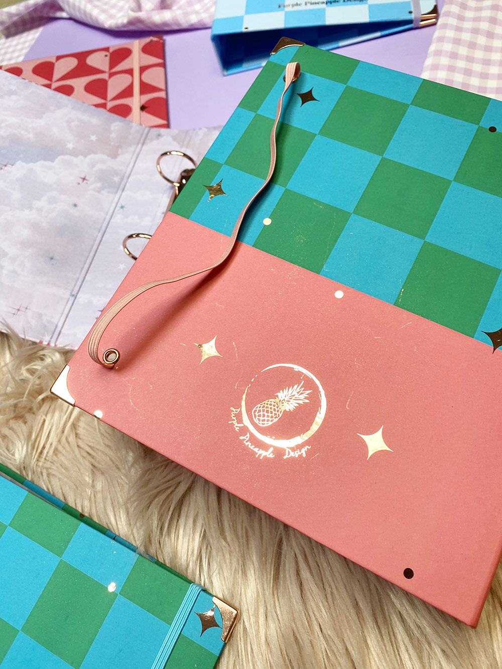 Pasta organizadora quadriculada verde e azul com aba rosa e desenho de ananás