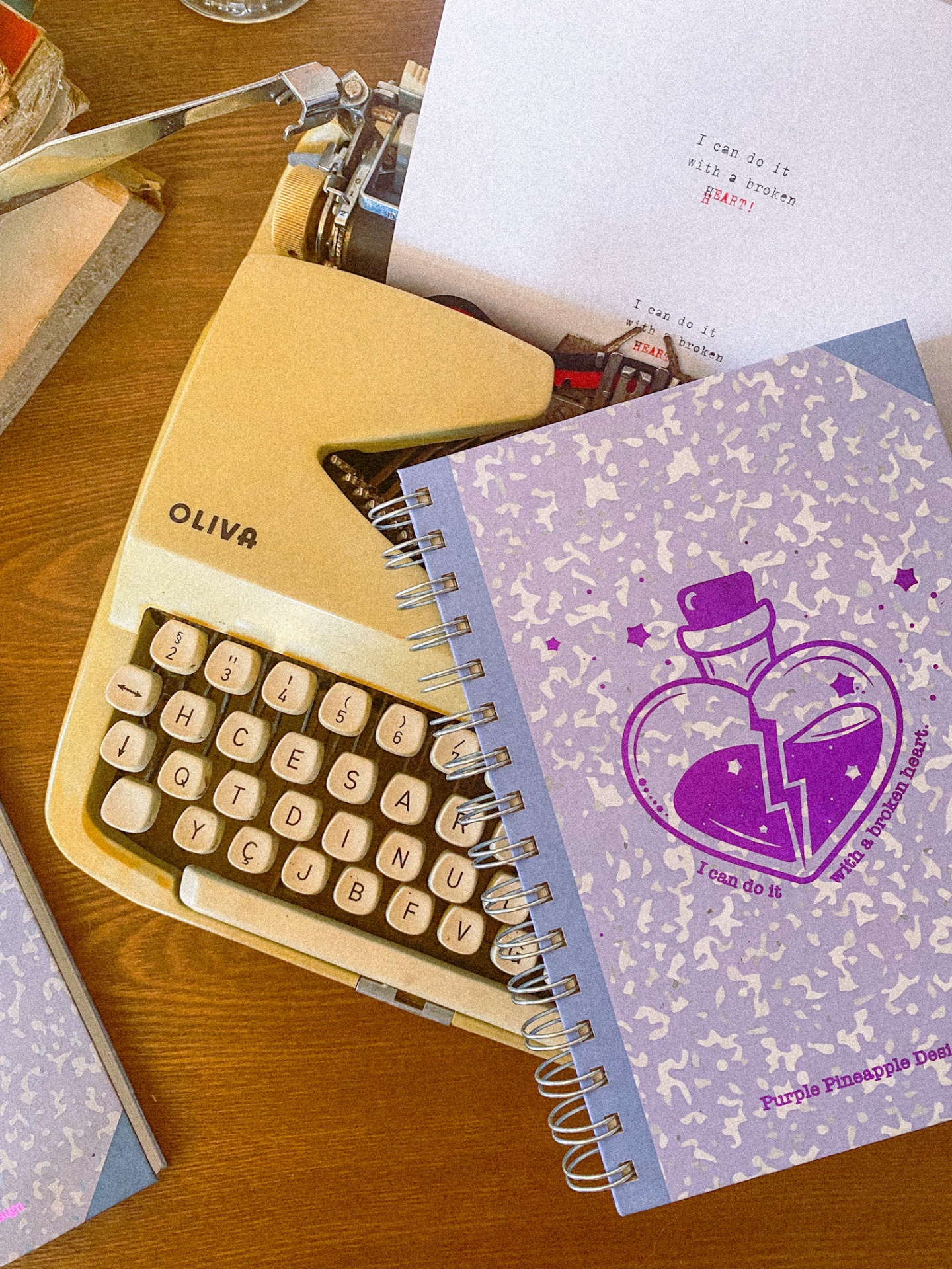 Máquina de escrever antiga amarela OLIVA com cadernos espirais cinza e ilustração roxa em cima