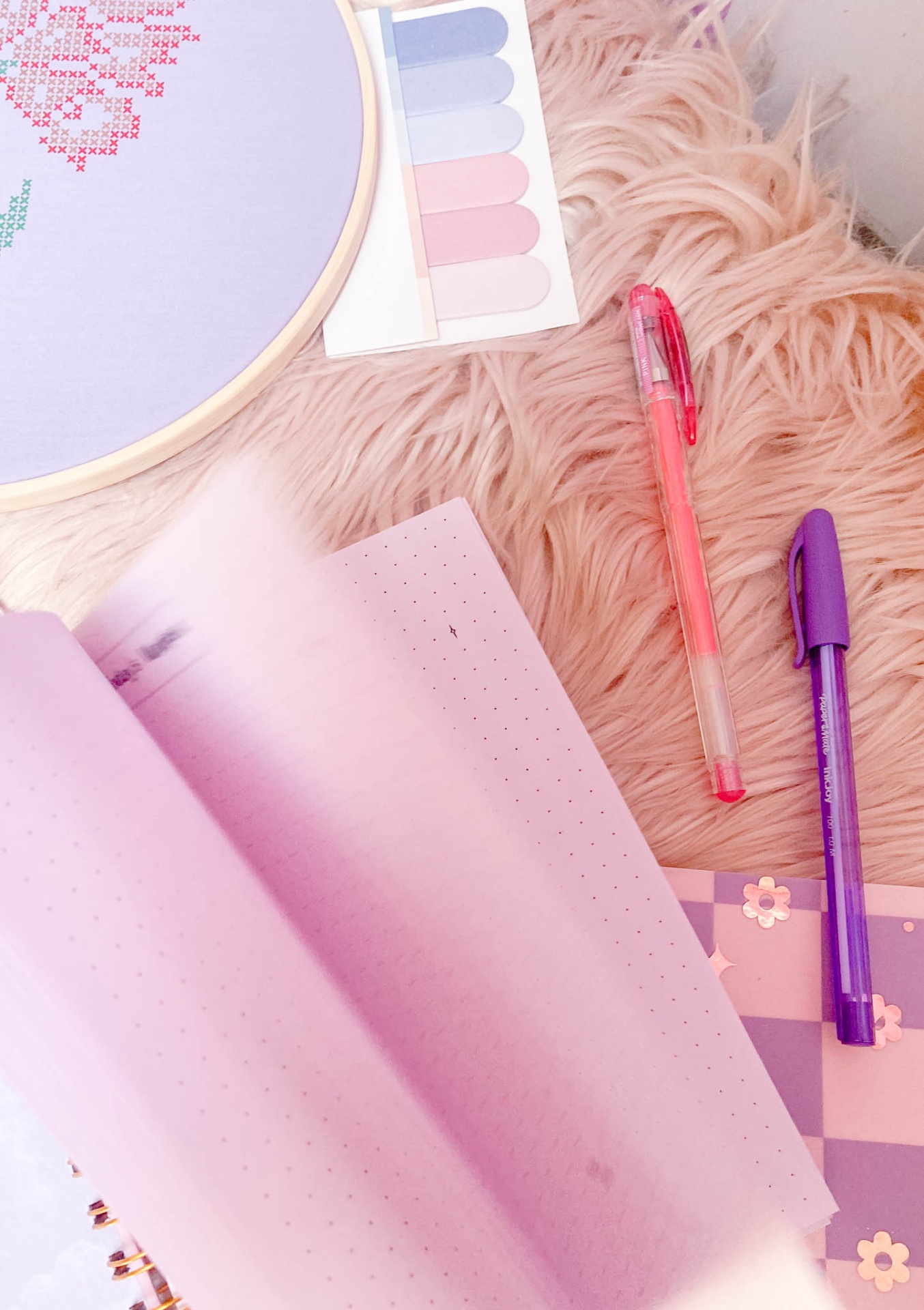 material de papelaria em tons rosa e lilás sobre tapete felpudo rosa