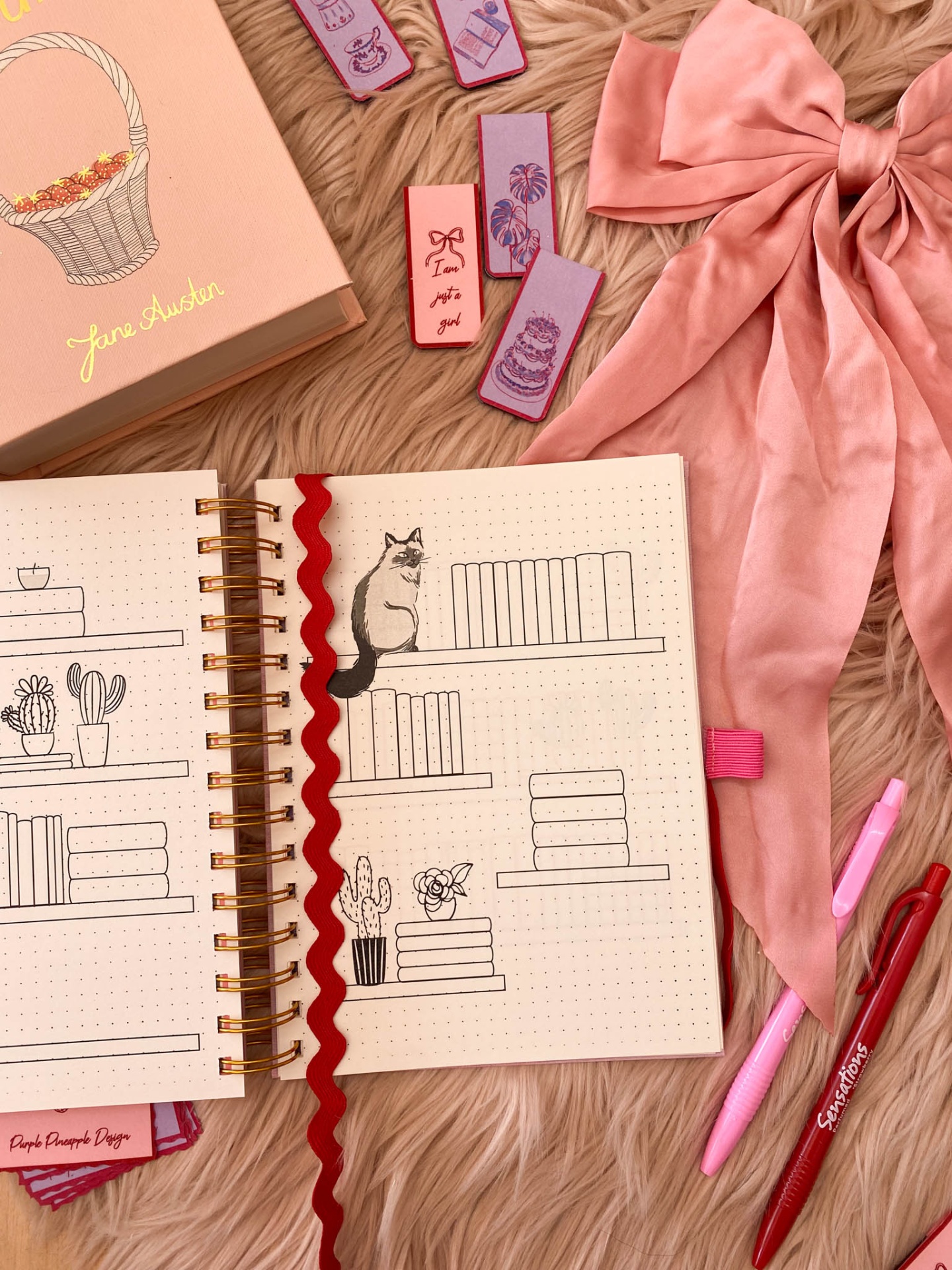 Caderno com desenhos, laço rosa, marcadores de livros, canetas e caixa 