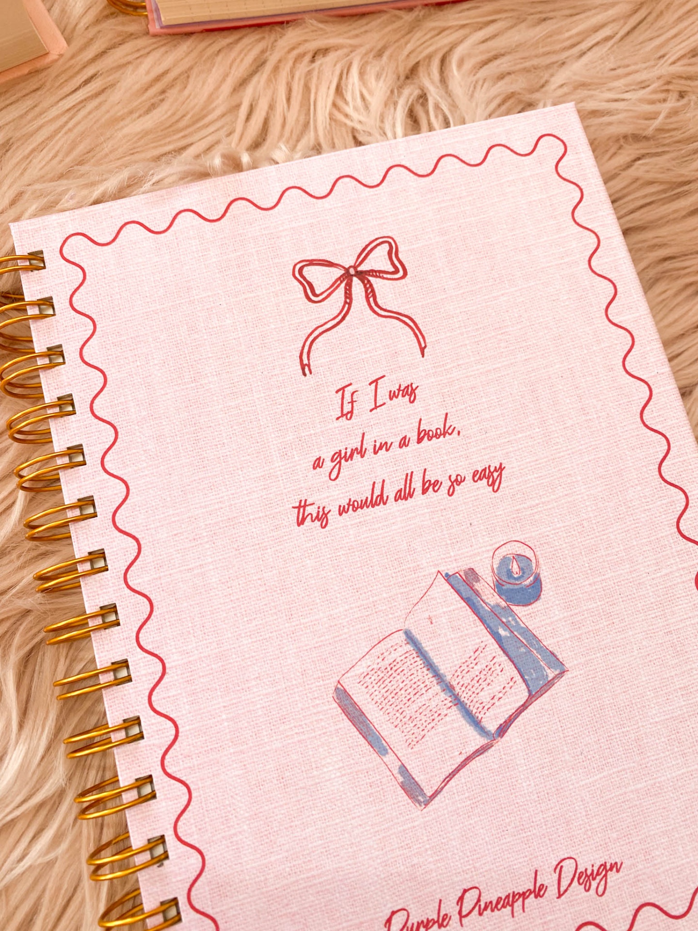 Caderno espiral rosa com ilustrações e texto em inglês sobre tecido peludo