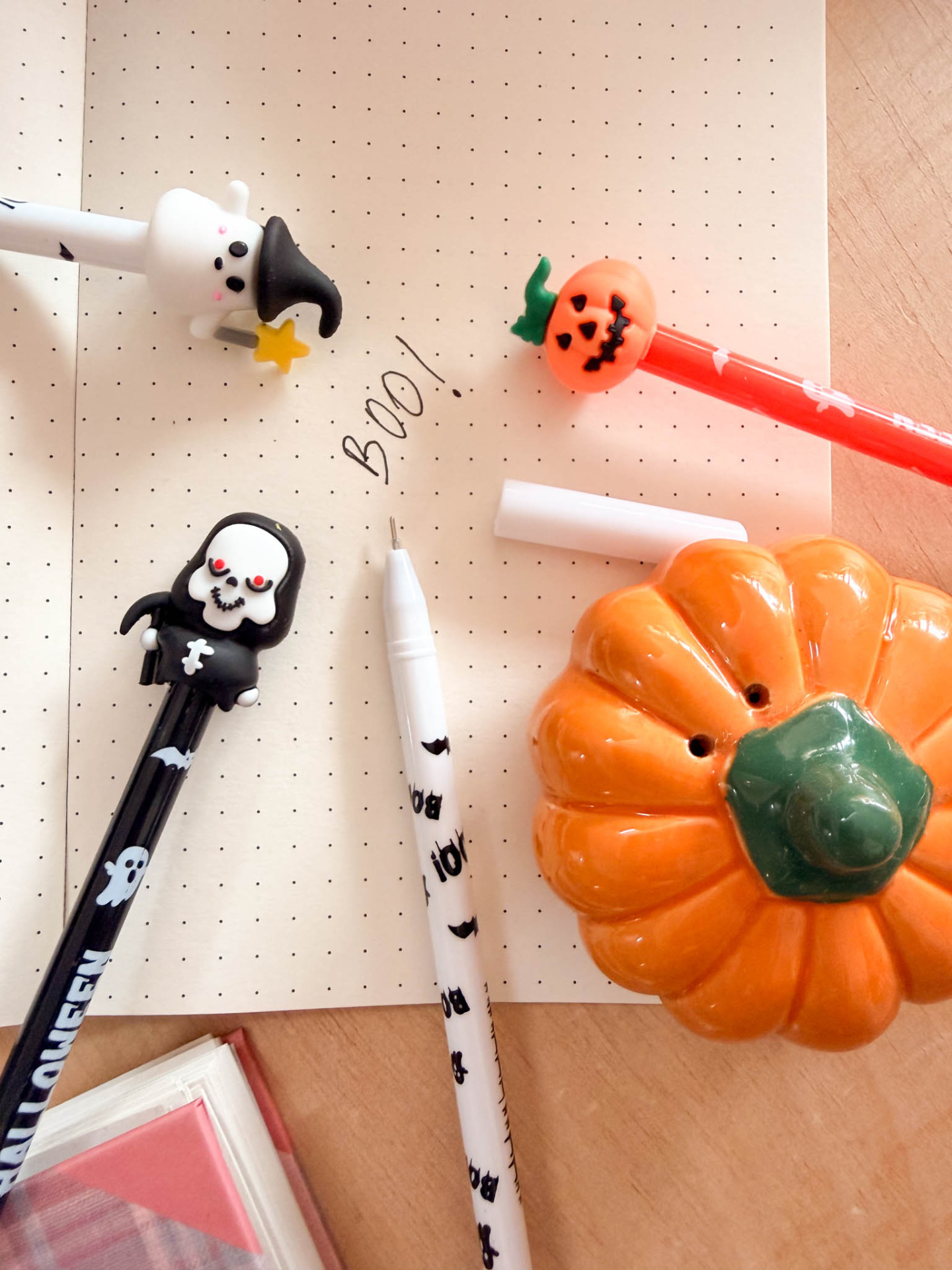 Canetas decorativas de Halloween e abóbora de cerâmica sobre caderno de pontos numa mesa