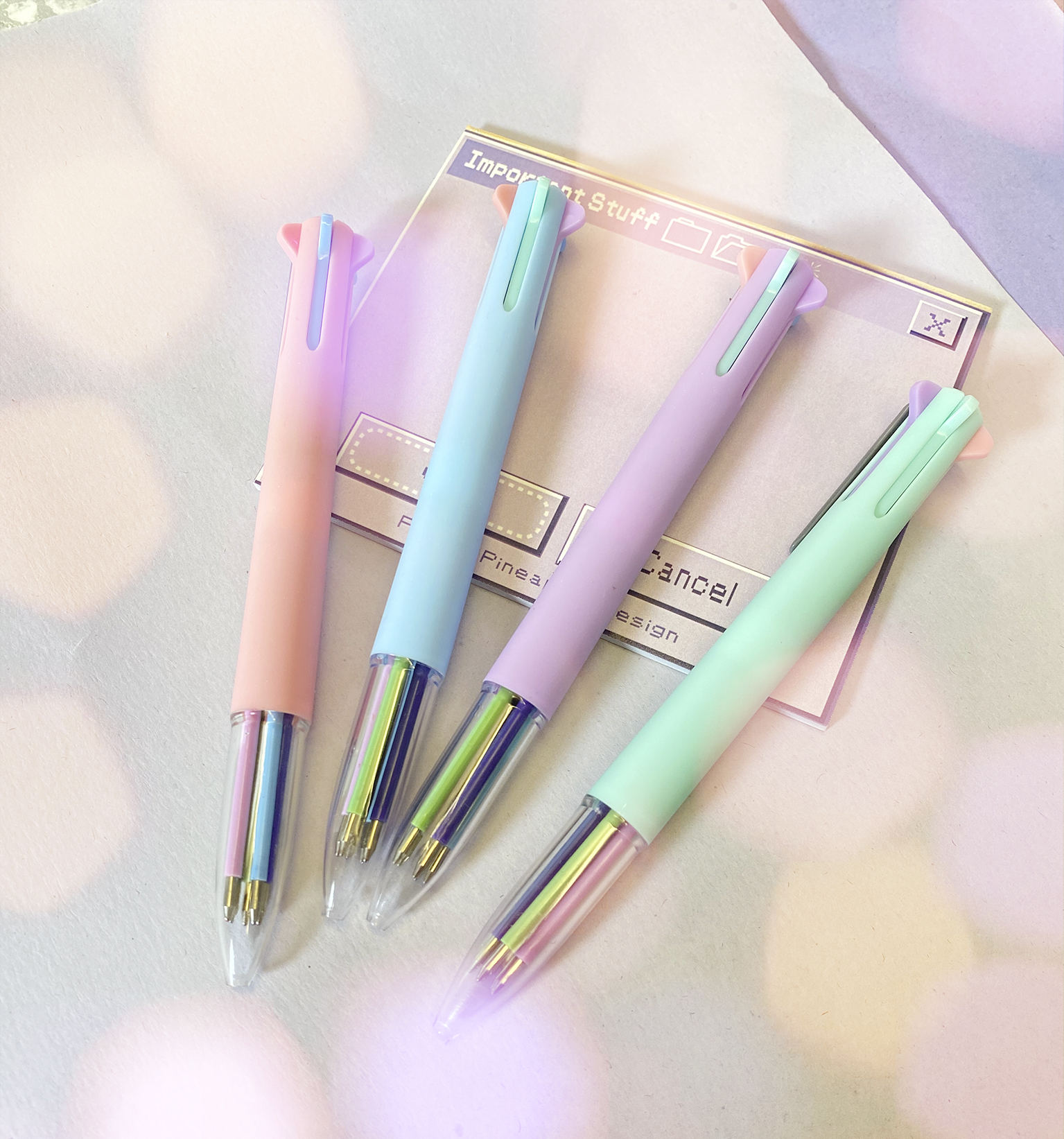 Quatro canetas pastel com partes metálicas e transparentes sobre fundo claro com texto digital