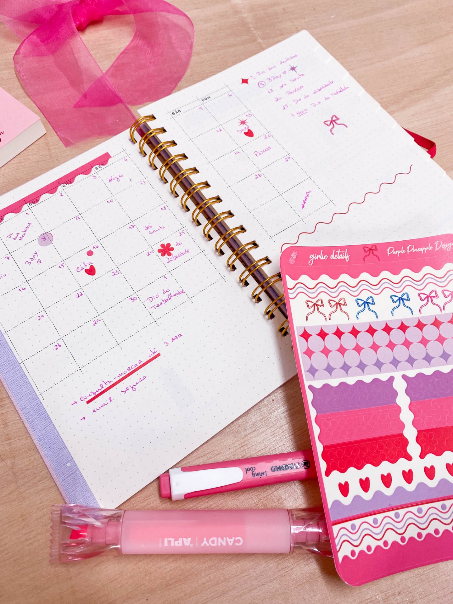 Agenda semanal com adesivos e marcador de texto cor-de-rosa sobre mesa de madeira clara