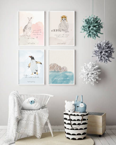 Quatro quadros de animais com texto em inglês numa parede branca acima de cadeira com manta e almofada e cesta com brinquedos