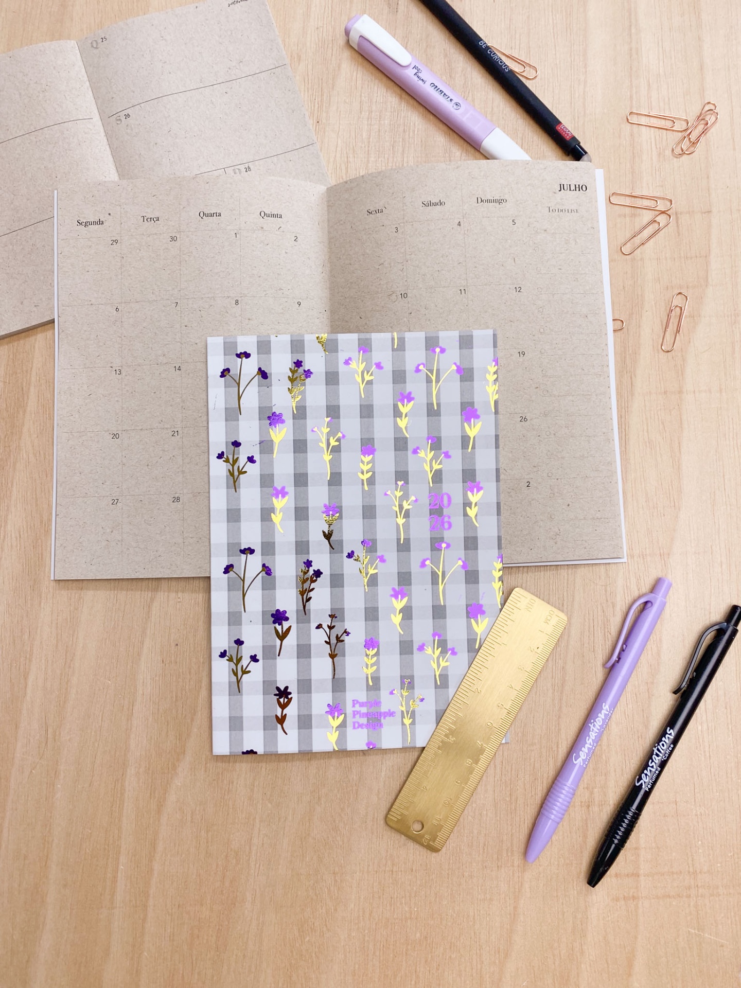 Planner semanal aberto com marcador de flores e material de escritório sobre mesa de madeira clara