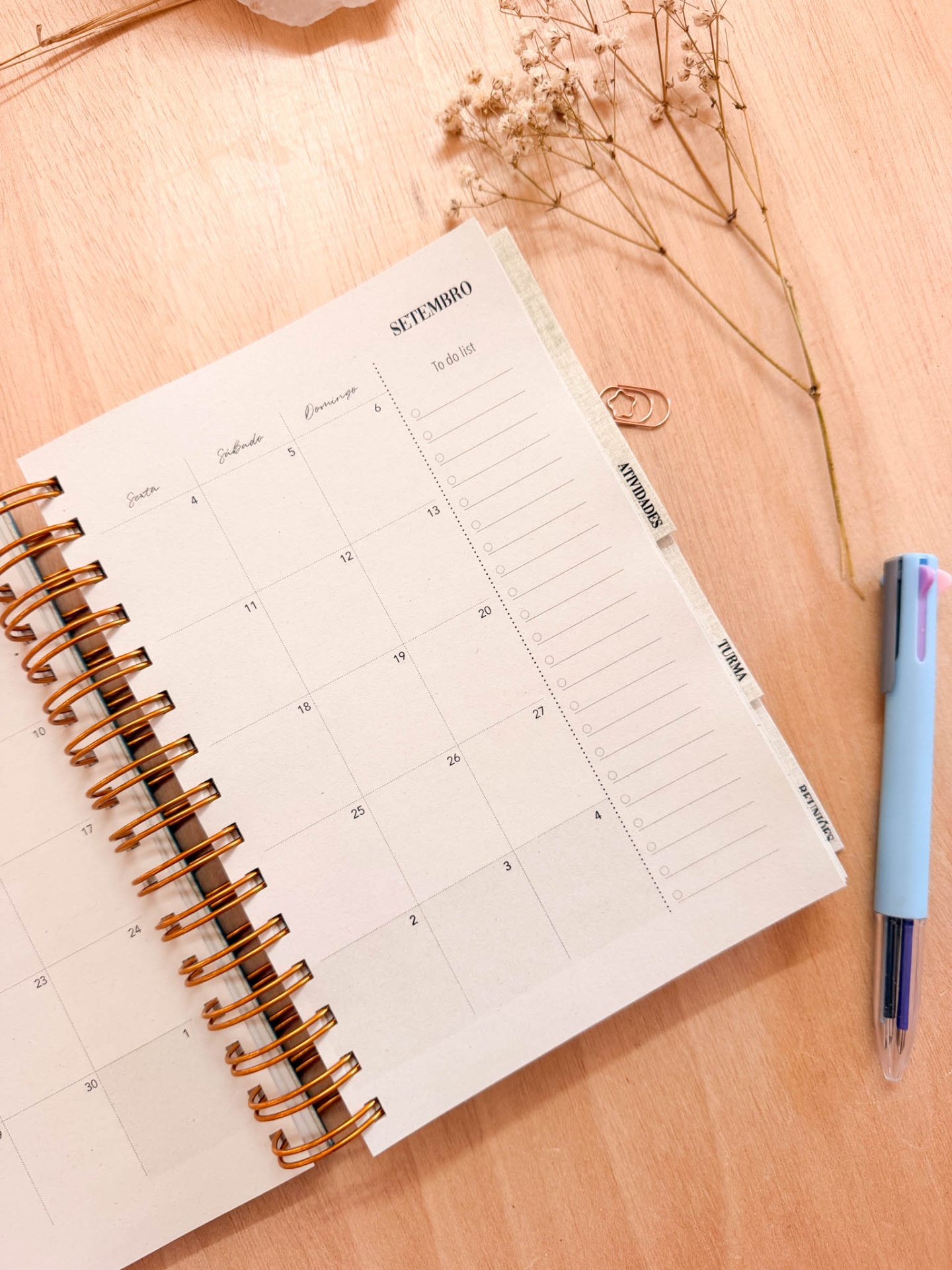 Agenda ou planner semanal com páginas creme e espiral dourada sobre mesa de madeira clara