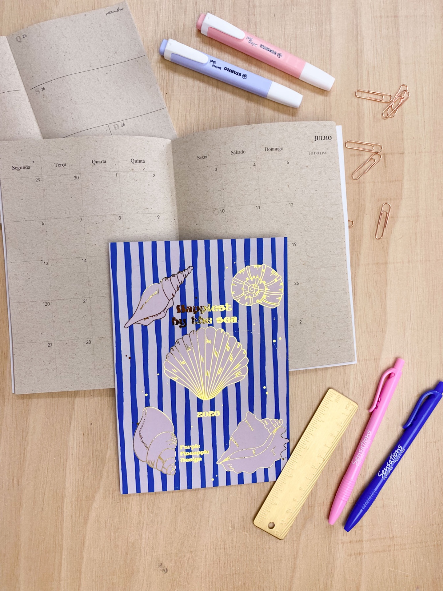 Material de escritório com cadernos, canetas, marcadores, régua e clips sobre mesa de madeira