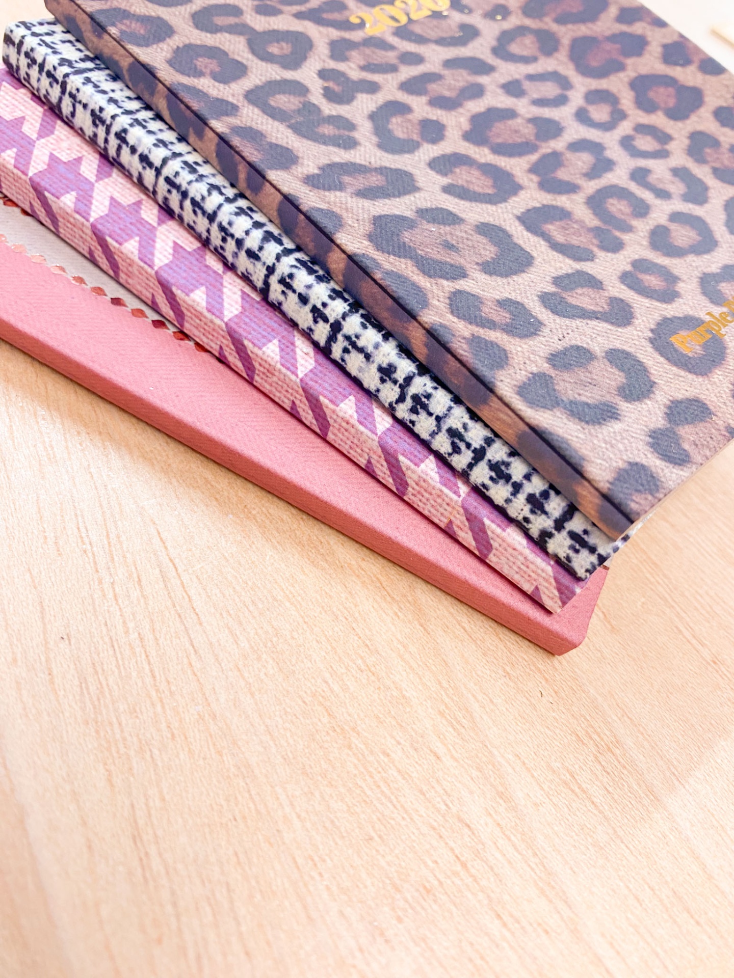 Quatro agendas com diferentes padrões e cores sobre uma mesa de madeira clara.