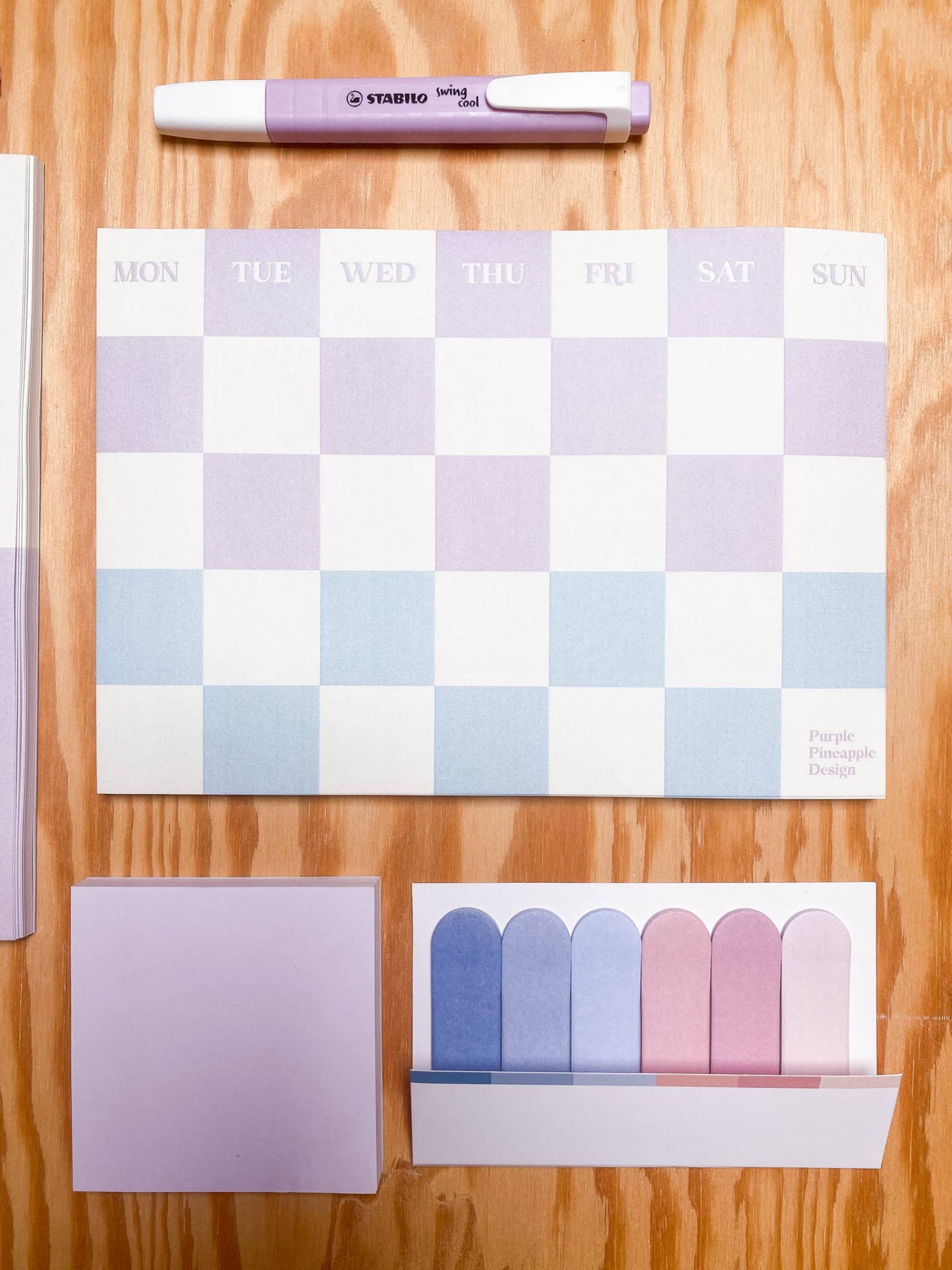 Calendário semanal com marcador e notas autocolantes em tons pastel sobre mesa de madeira