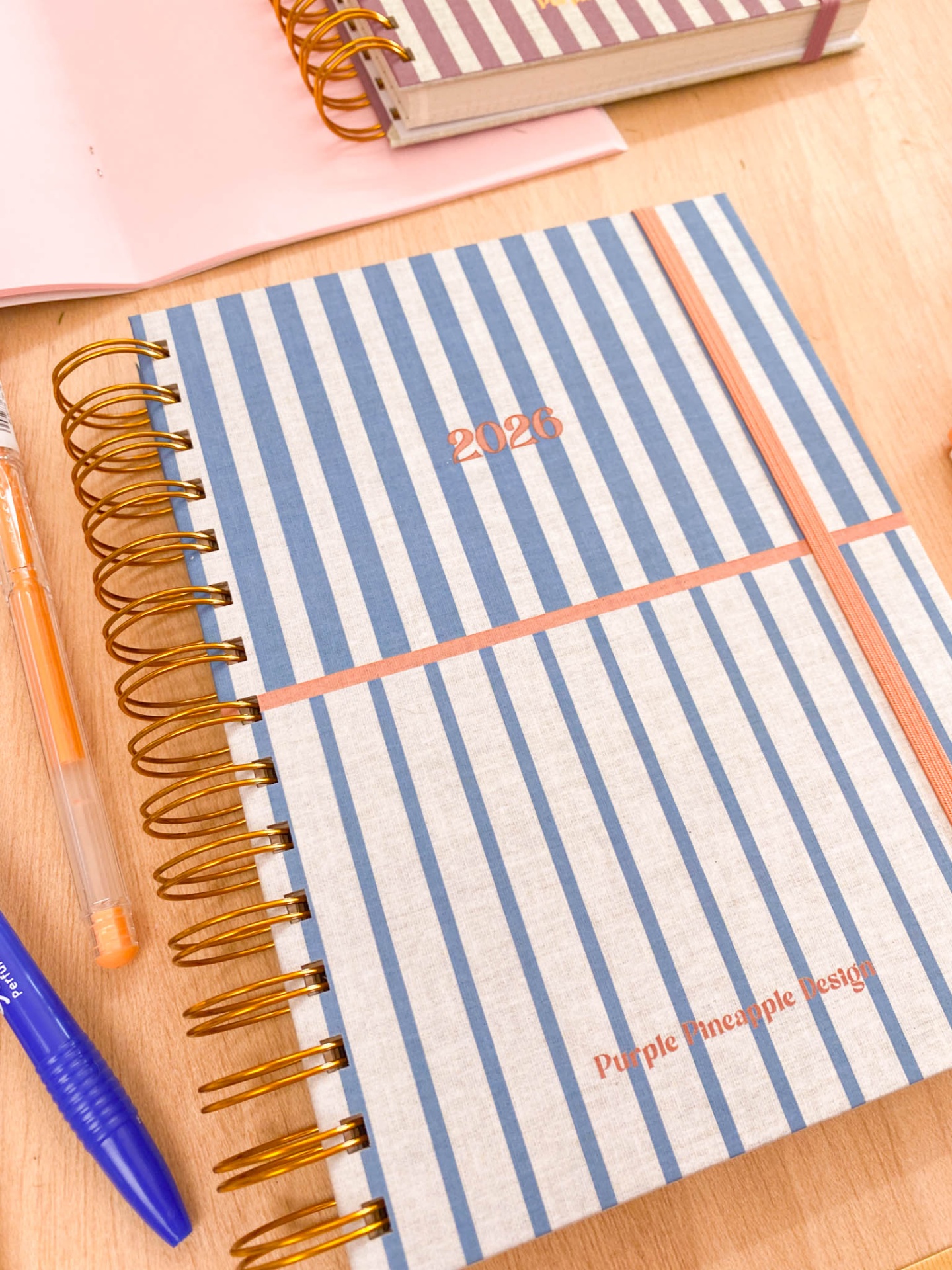 Caderno espiral riscado azul e branco com canetas