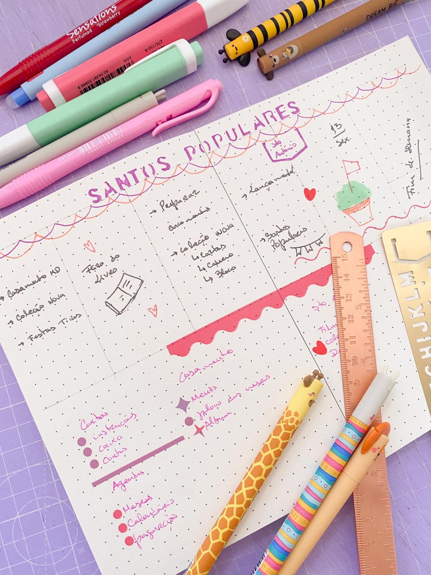 Como decorar o teu diário com inspiração nos Santos Populares 🎉 Folha com planejamento manuscrito com canetas coloridas, lápis e régua numa mesa lilás.