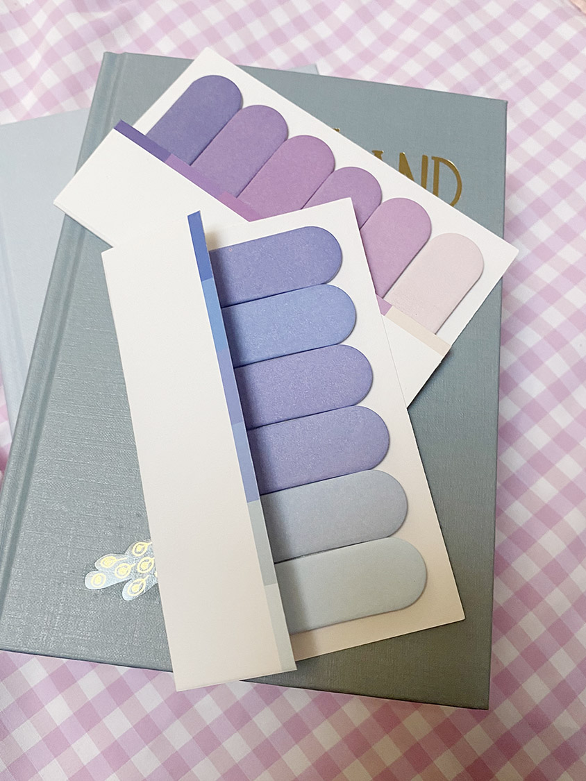 Cartelas de autocolantes em vários tons de roxo sobre um livro cinzento, fundo rosa xadrez.