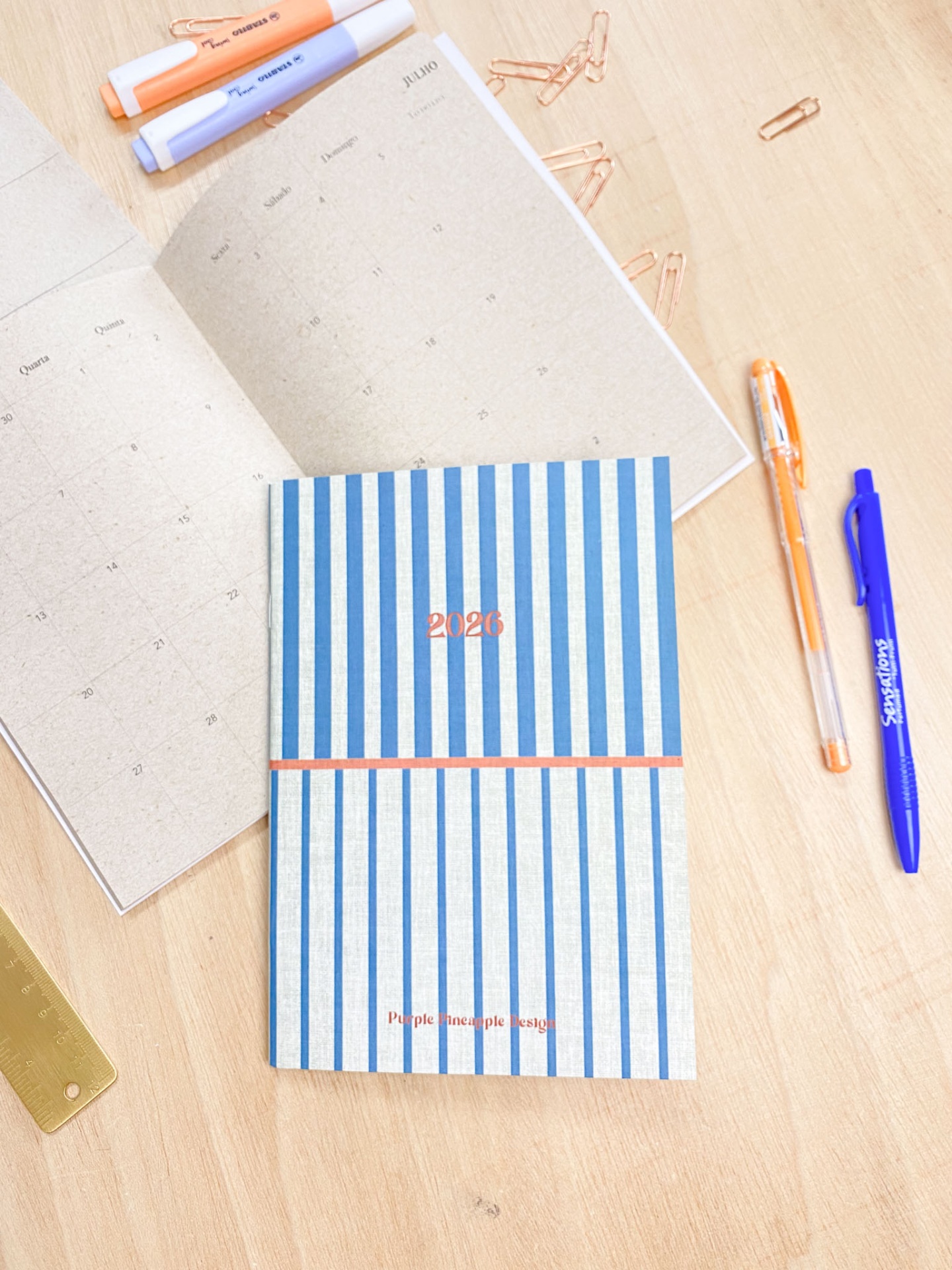 Agenda 2020 com riscas azuis e brancas e canetas sobre mesa