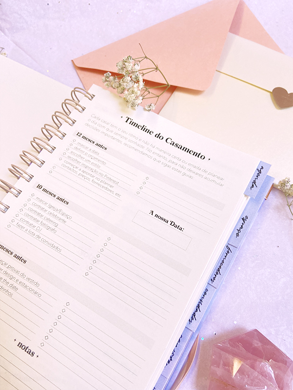 Planner aberto em página de planejamento de casamento com envelope e flores secas ao redor