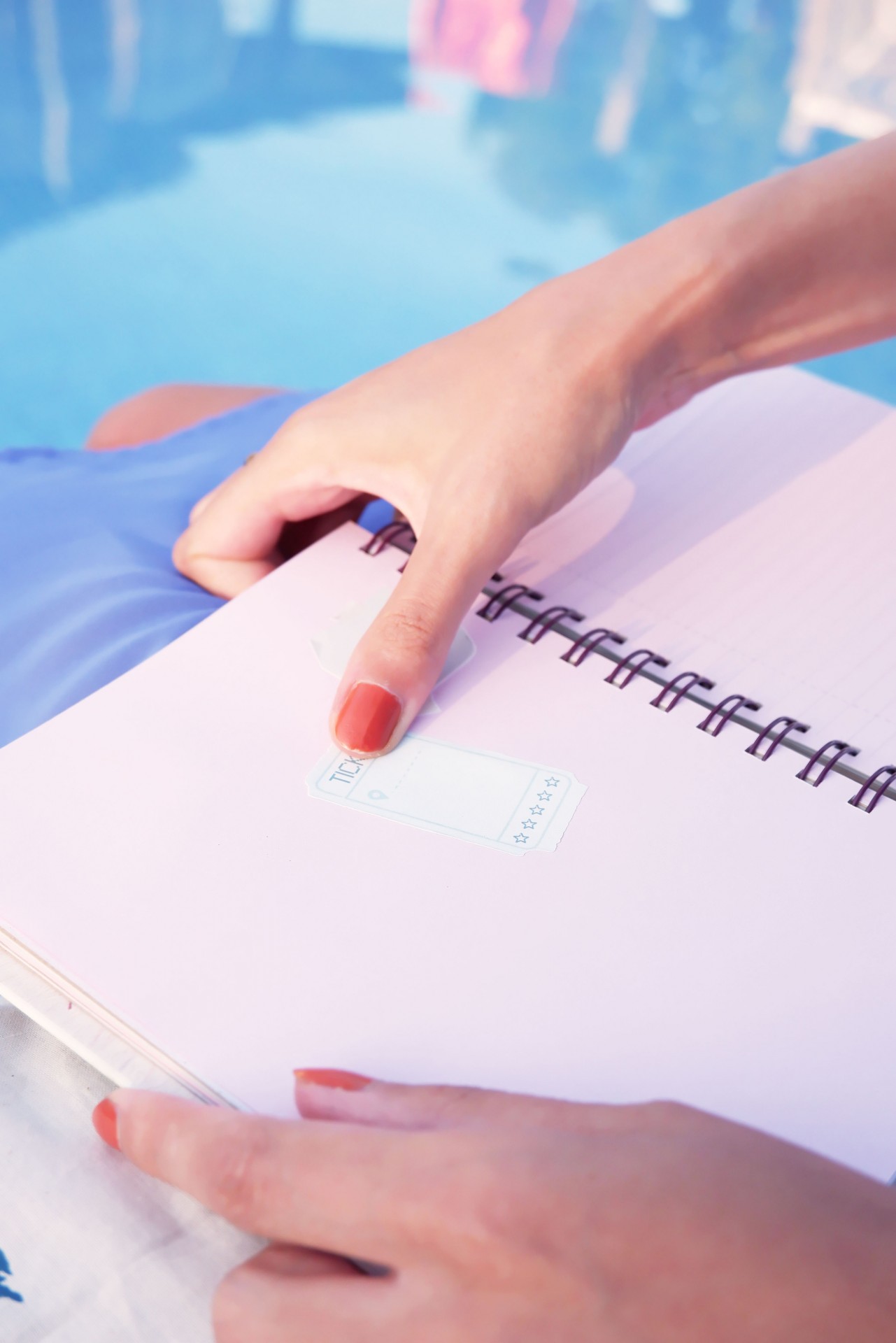 Mãos segurando caderno espiral branco com etiqueta de avaliação e fundo de piscina azul