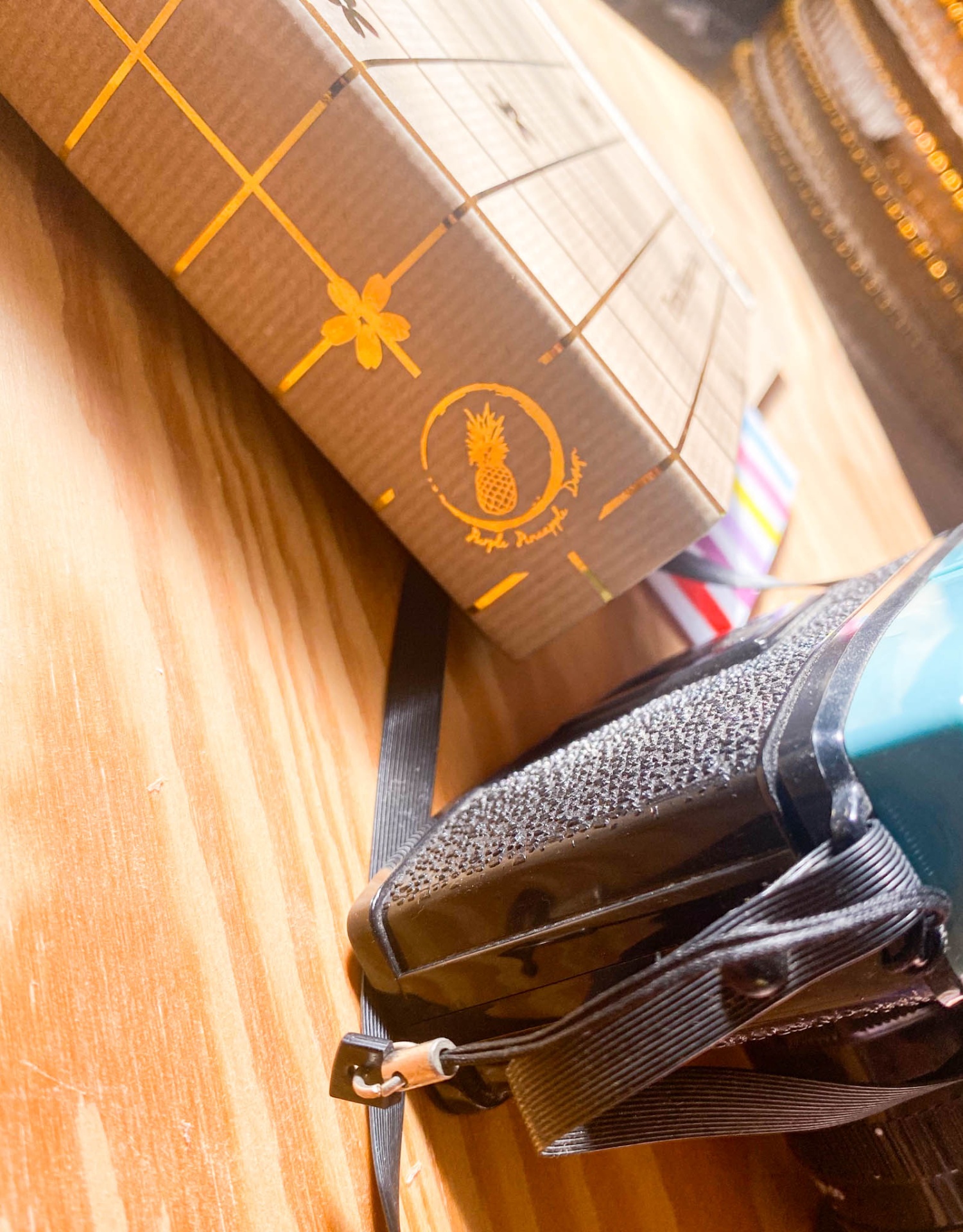 Caixa de cartão com design listrado e símbolo de abacaxi junto de uma câmara fotográfica