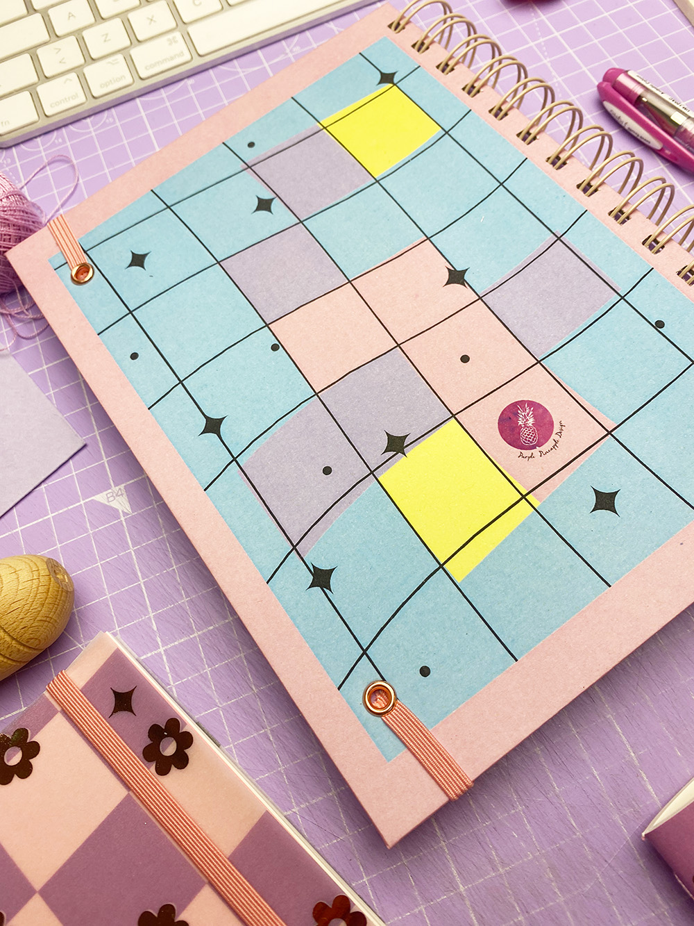 Cadernos coloridos em espiral com padrões geométricos em superfície lilás