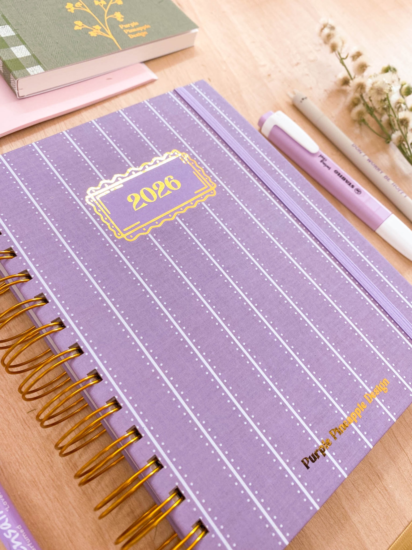 Caderno lilás com espiral dourado e texto 2026