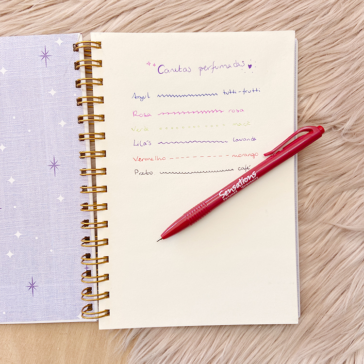 Notebook lilás com estrelas, páginas brancas com escrita colorida e caneta vermelha sobre superfície peluda bege