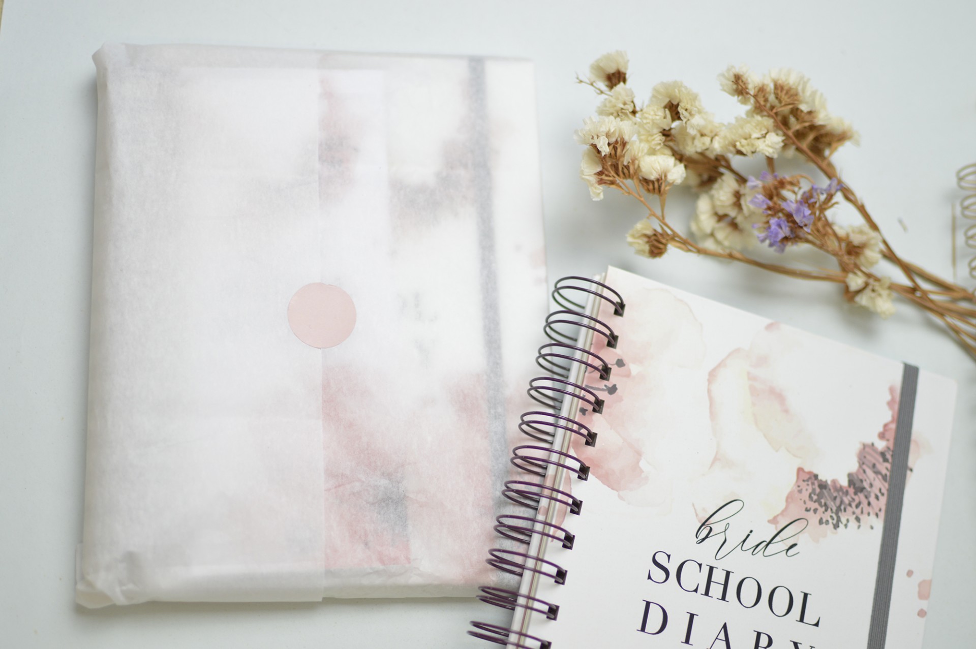 Diário escolar branco com detalhes em rosa e folhas secas ao lado