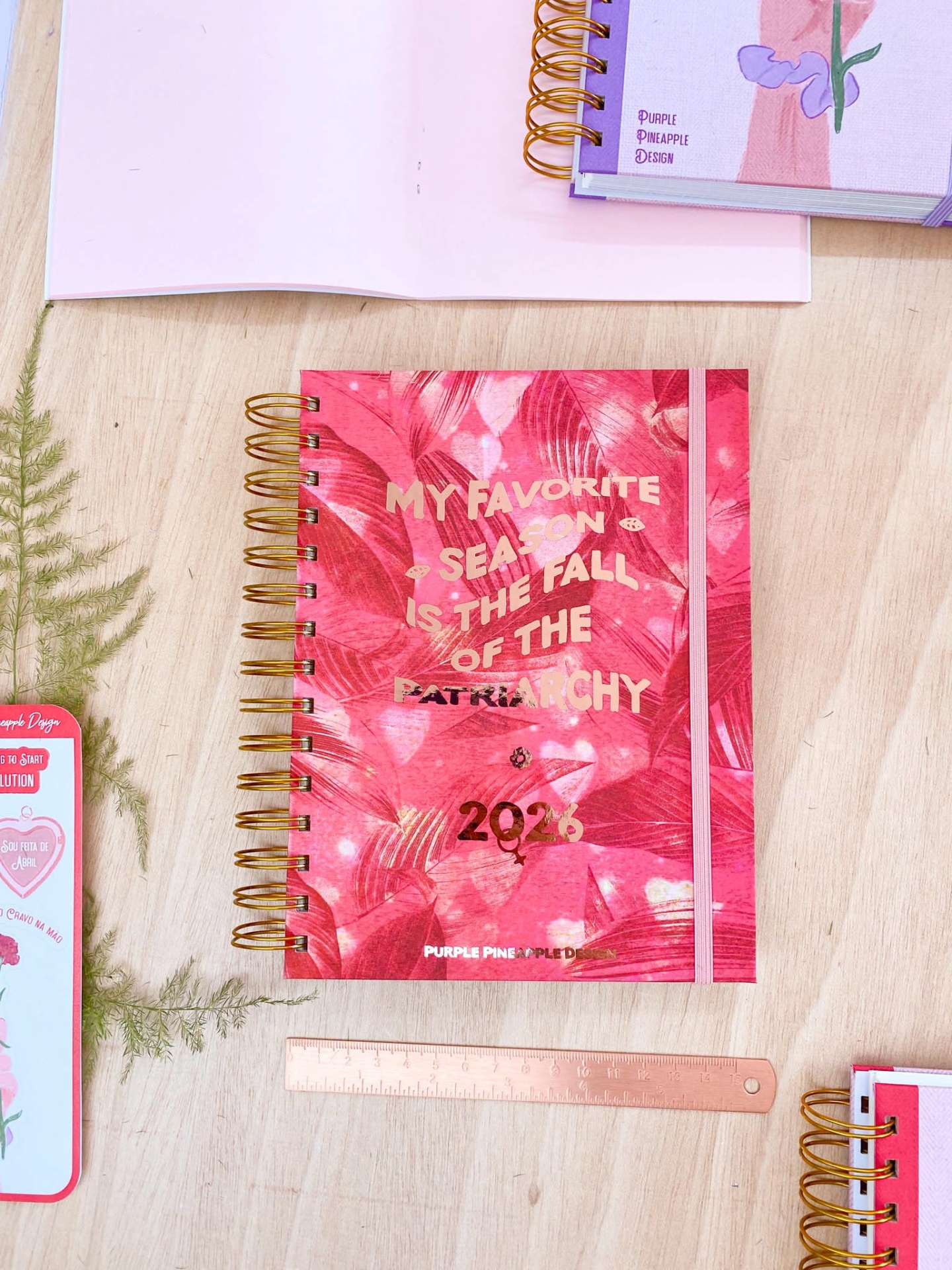Caderno espiral vermelho com padrão floral e texto dourado sobre mesa clara