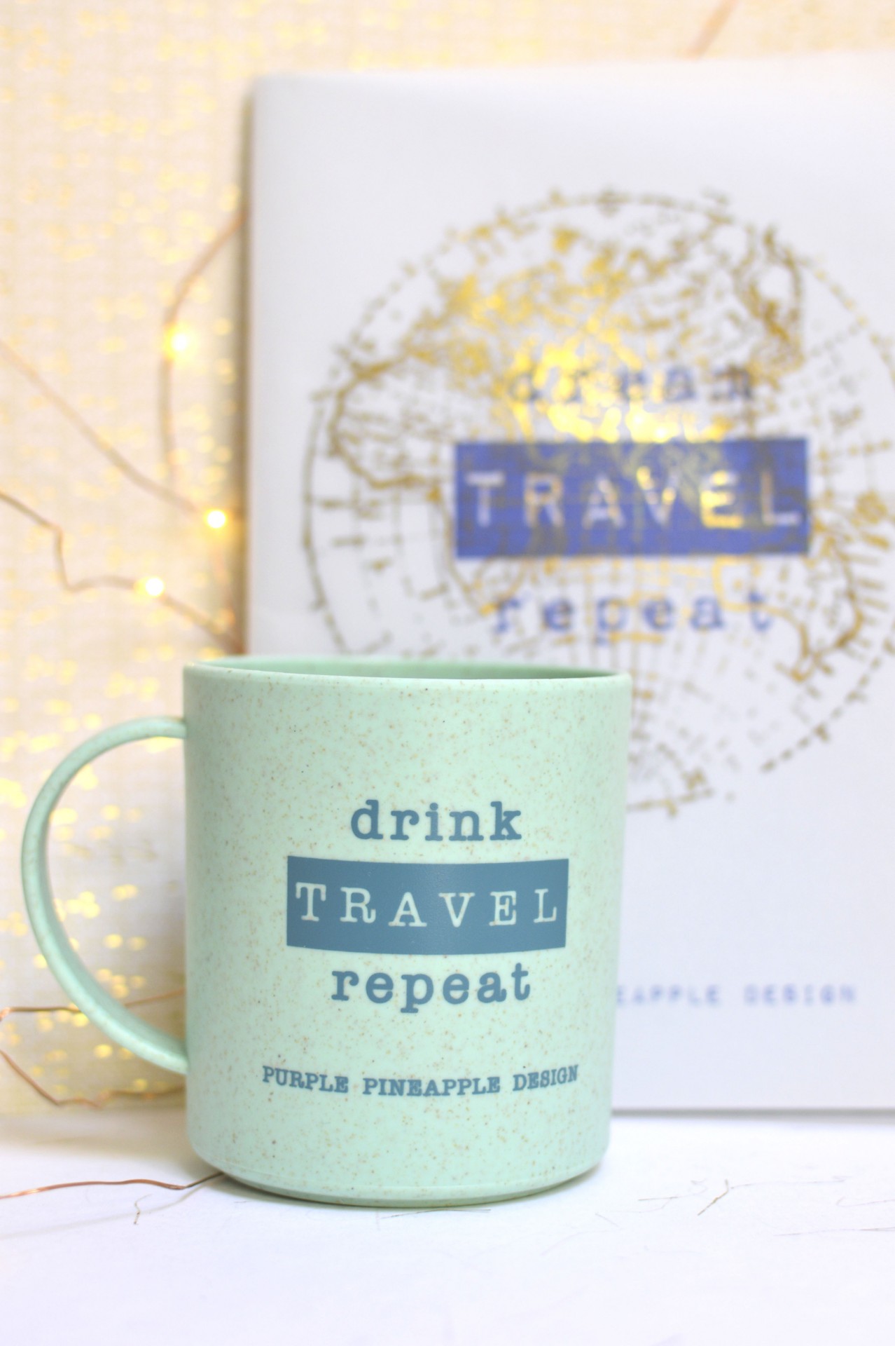 Caneca verde com texto azul e fundo branco com mapa dourado e luzes de fada amarelas