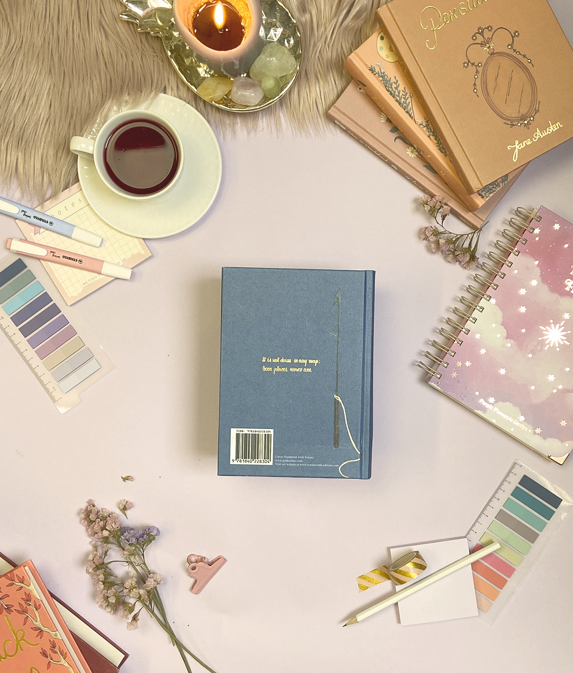 Mesa com cadernos, paletas de cores, chávena com chá e vela acesa