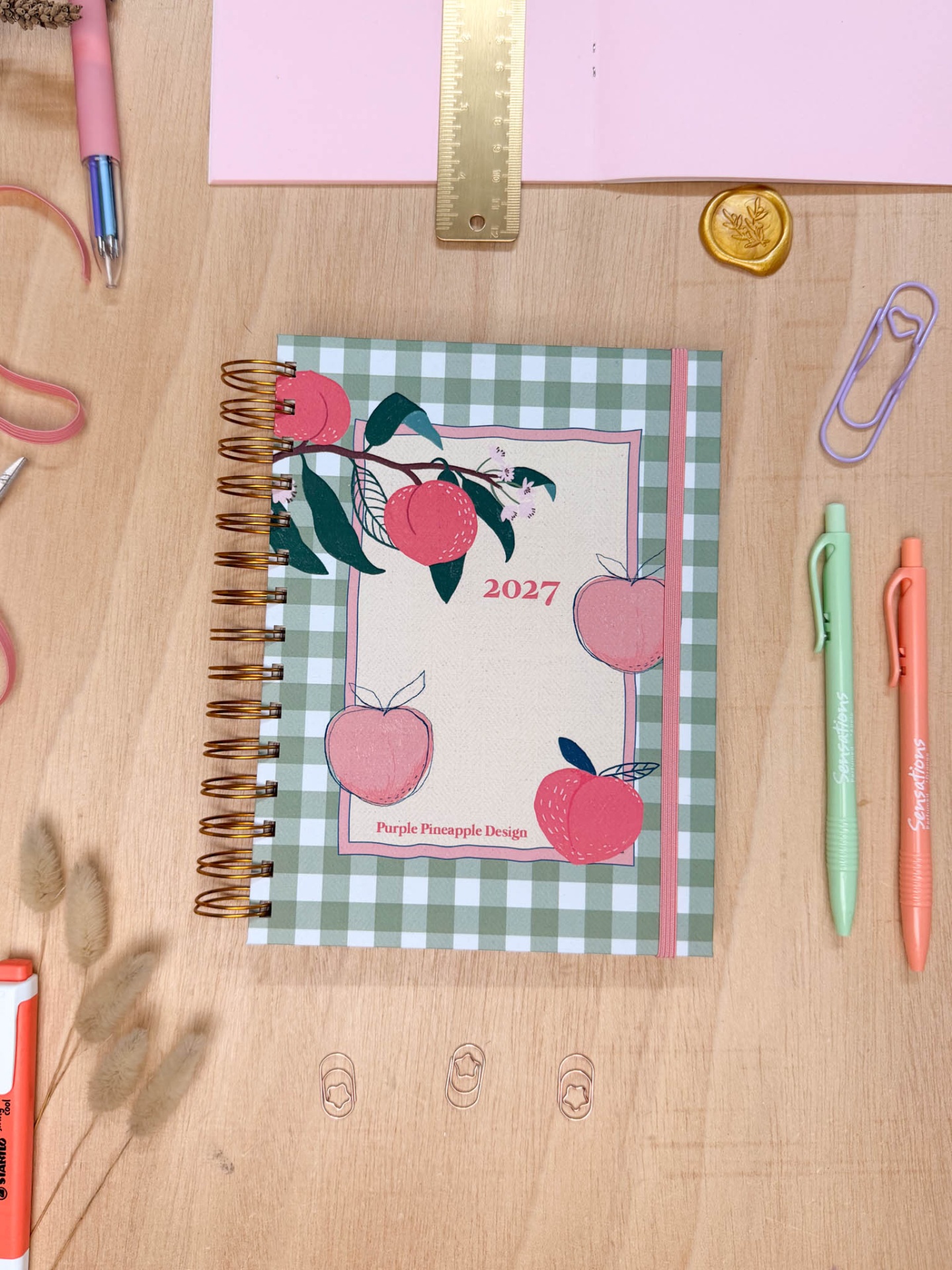 Agenda 2027 com capa quadriculada verde e branco decorada com pêssegos e maçãs cor-de-rosa