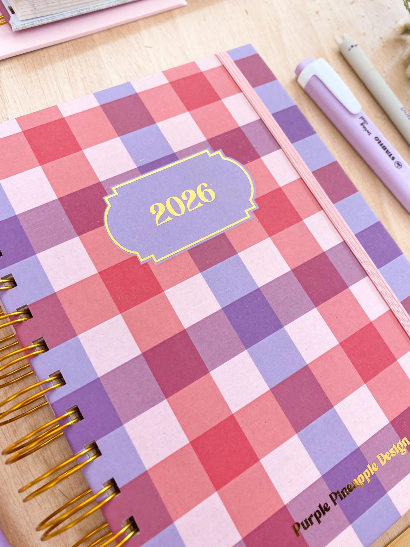 agenda quadriculada 2026 com espiral dourada e elástico rosa
