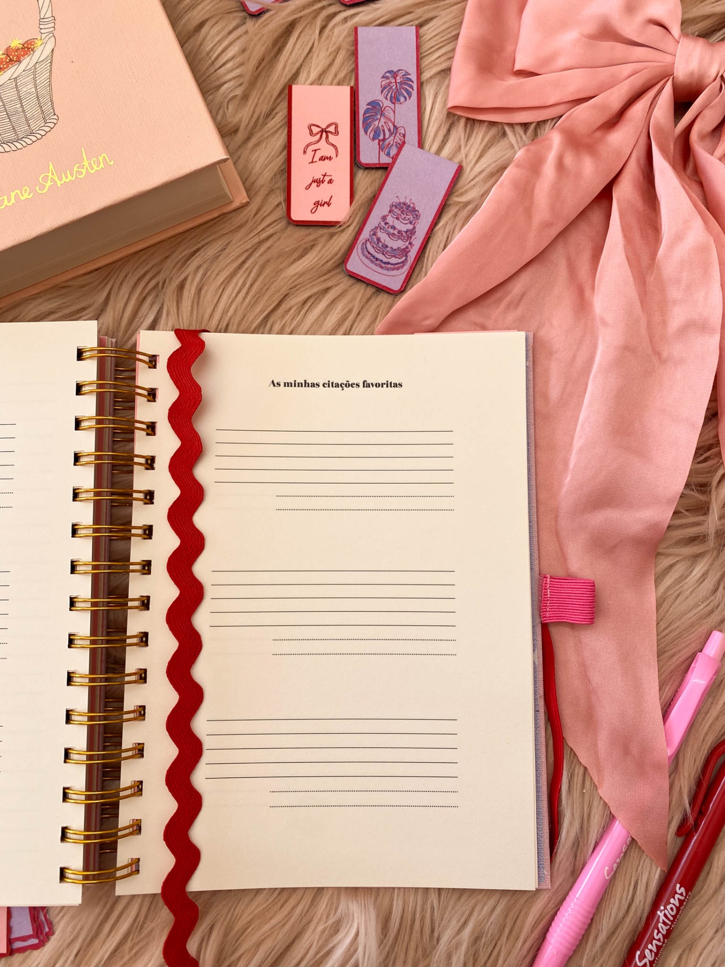 Caderno aberto com marcador vermelho e laço rosa sobre superfície felpuda
