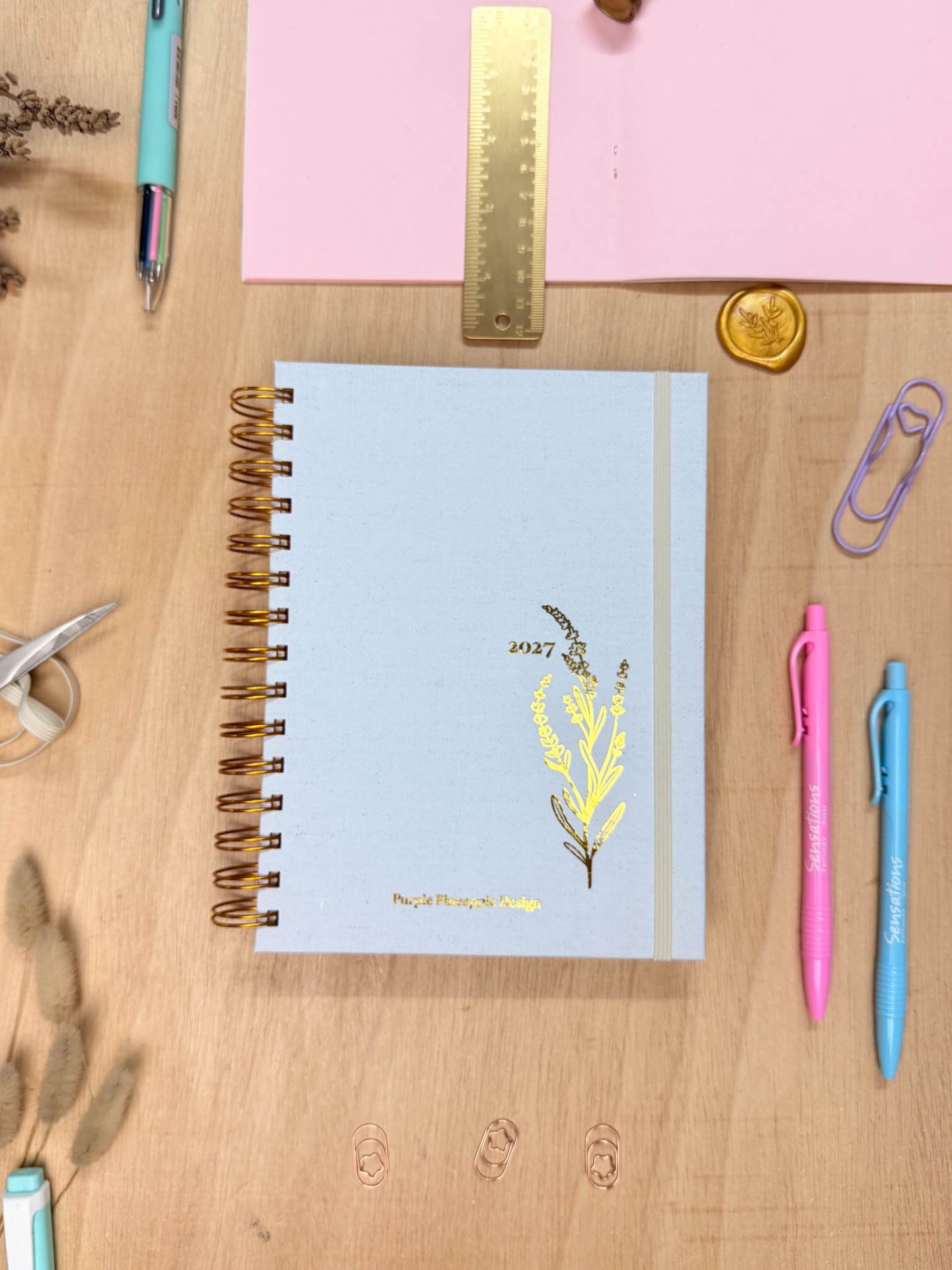 Caderno azul com detalhes dourados e papelaria sobre mesa de madeira