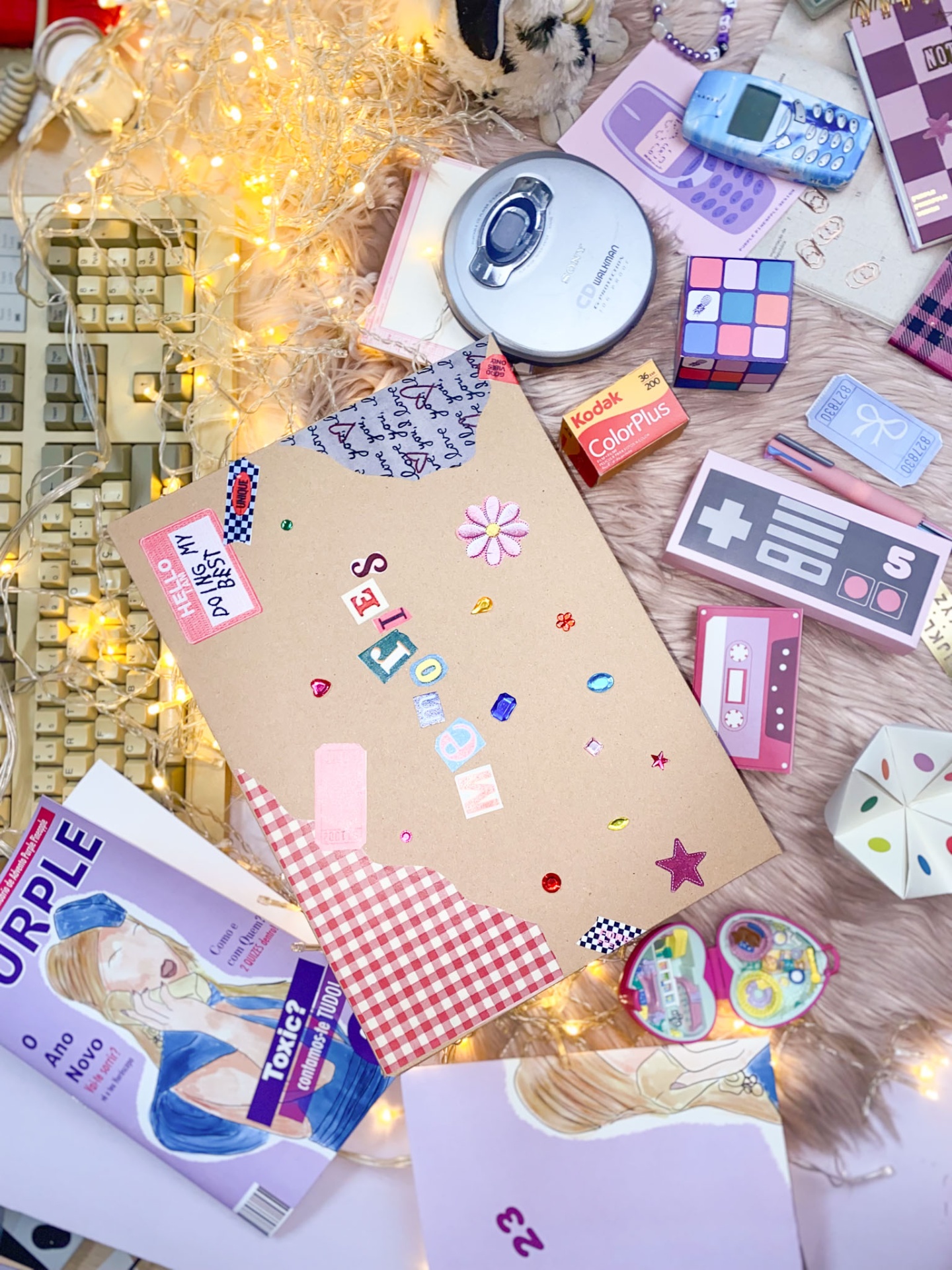 Caderno decorado com adesivos e padrão xadrez, rodeado por objetos vintage e luzes